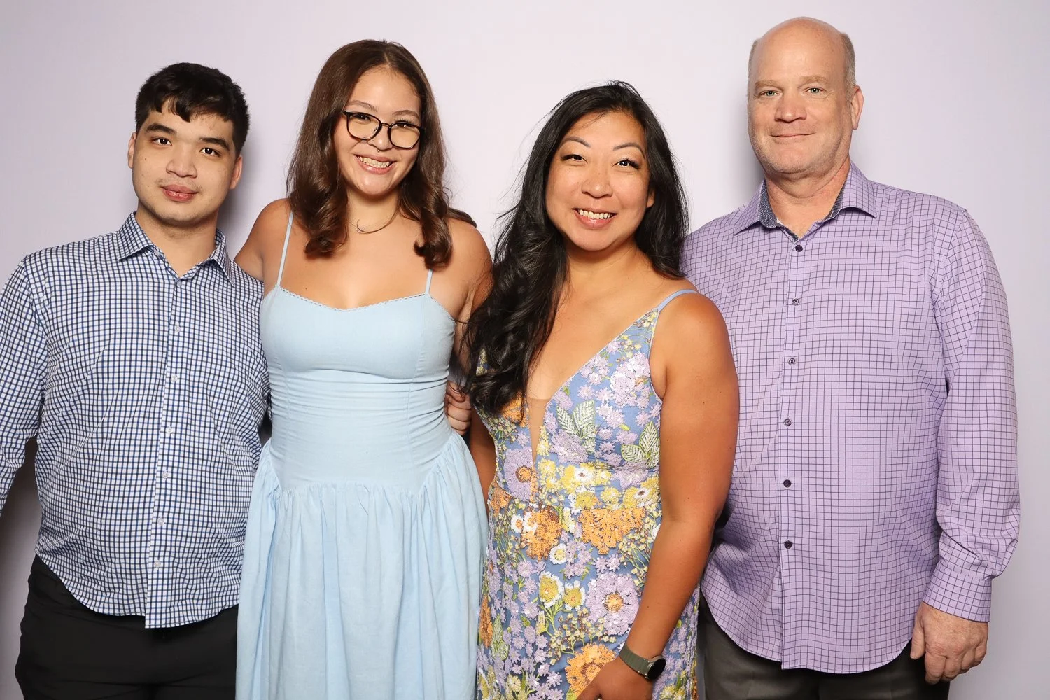 Group of four people, two women and two men, smiling and standing close together in front of a plain background.
