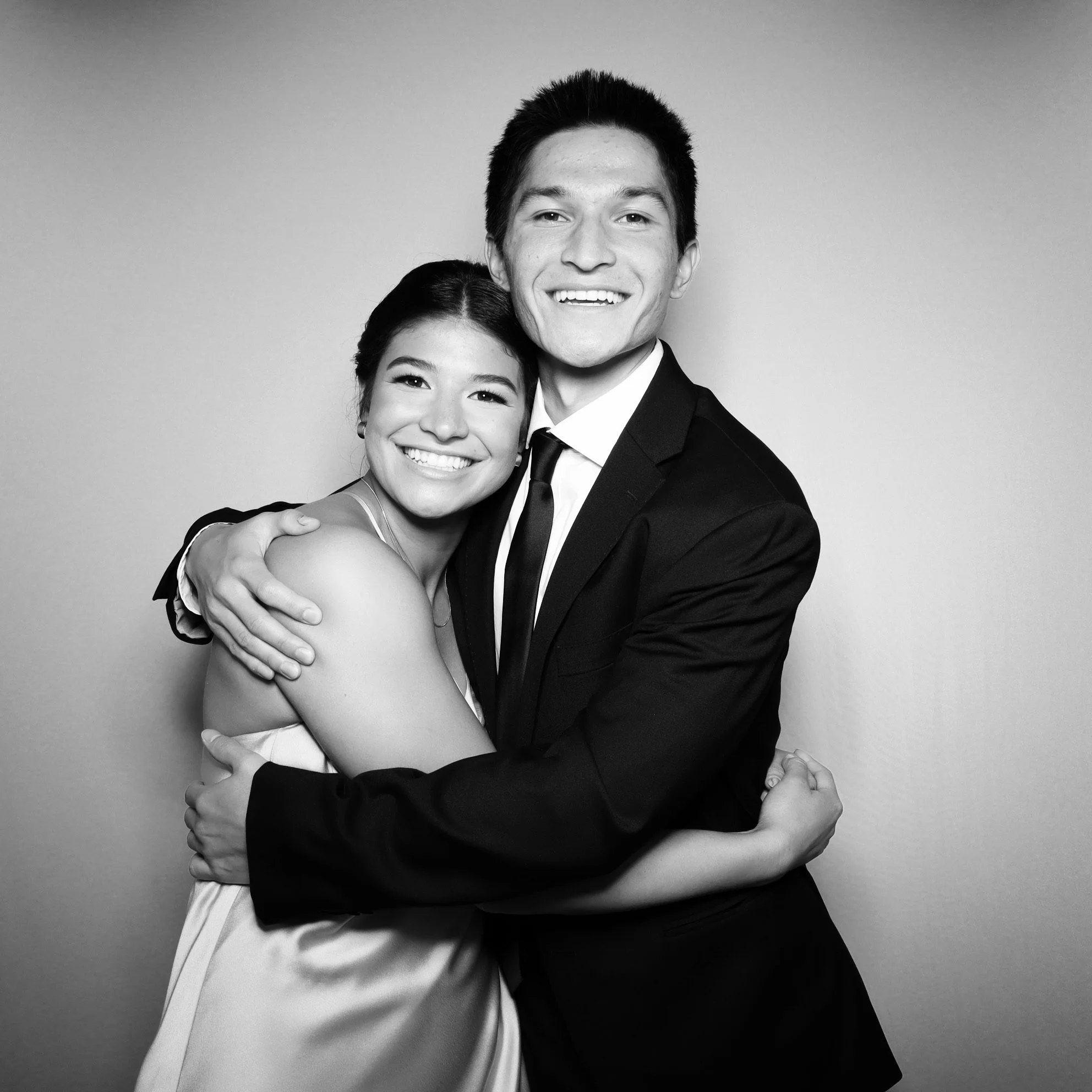 A black-and-white photo of a smiling couple hugging, with the woman wearing a dress and the man in a suit and tie.