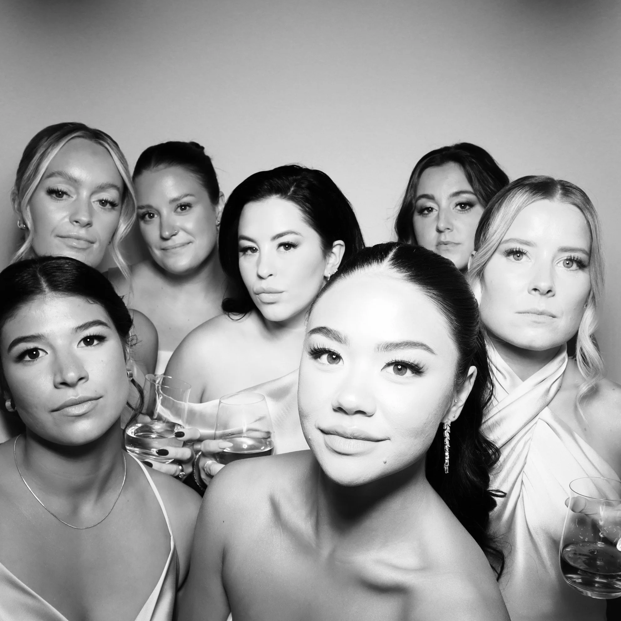 Black and white photo of seven diverse women posing together, some holding glasses of water, with neutral expressions.