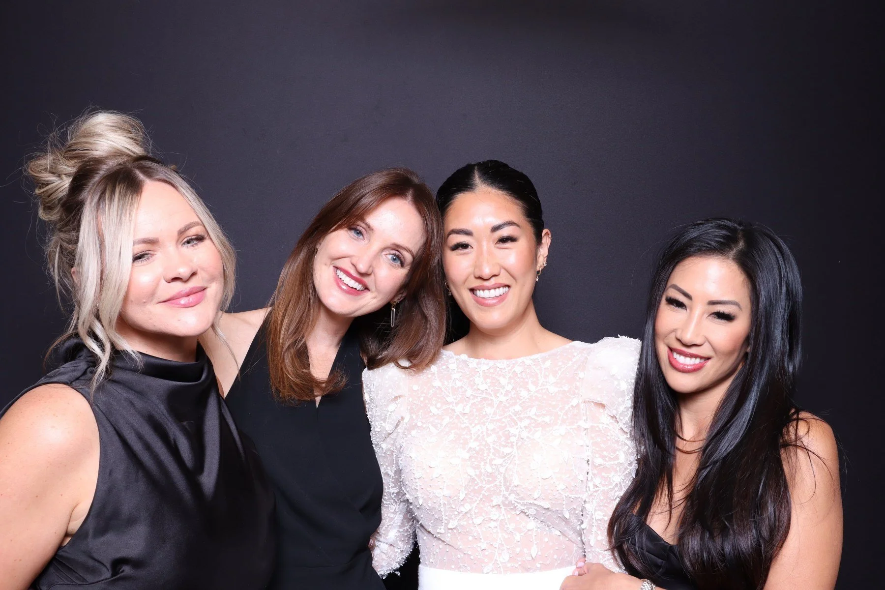 Four women smiling together in front of a black background.