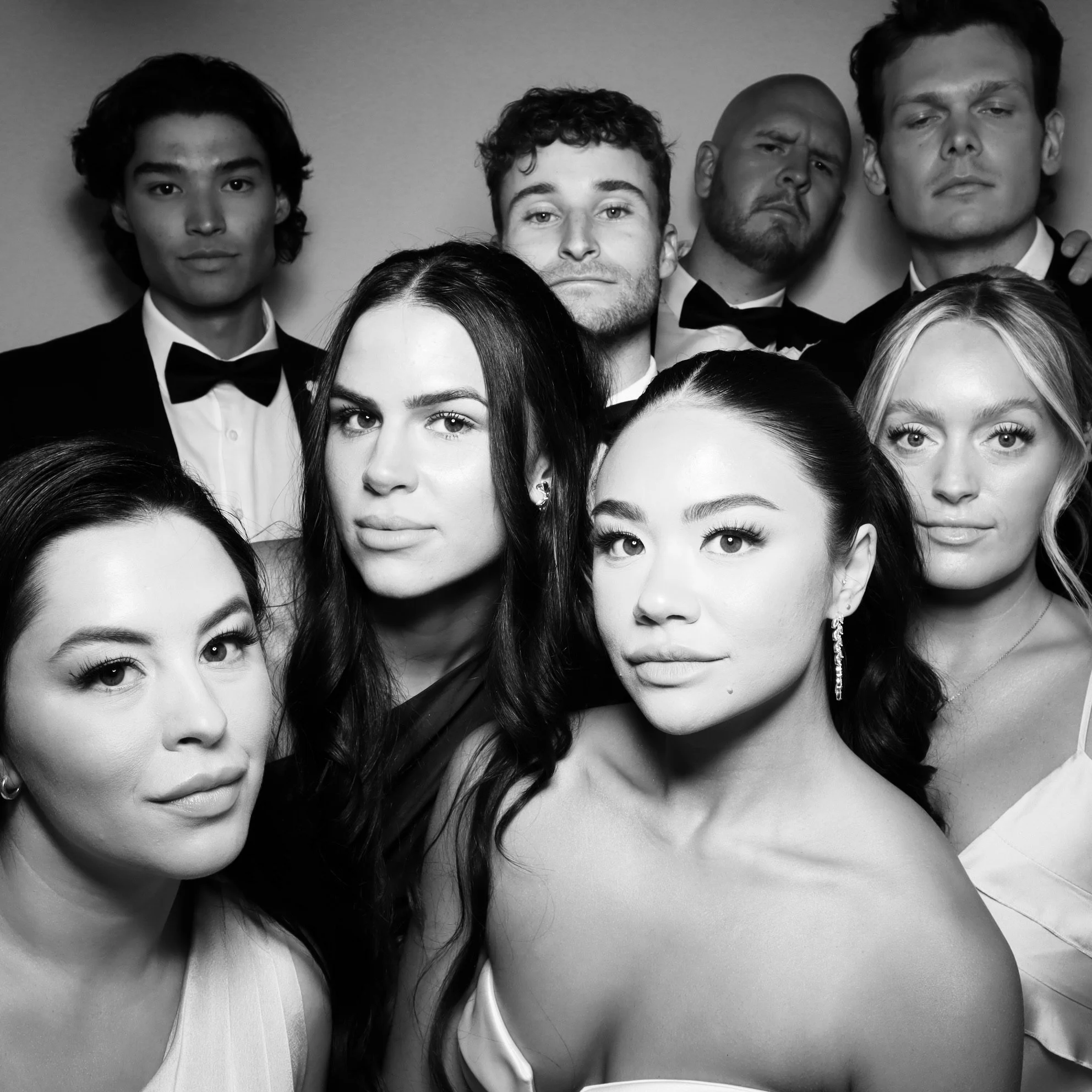 Black and white photo of a group of nine young adults dressed in formal attire, posing closely for a group portrait.