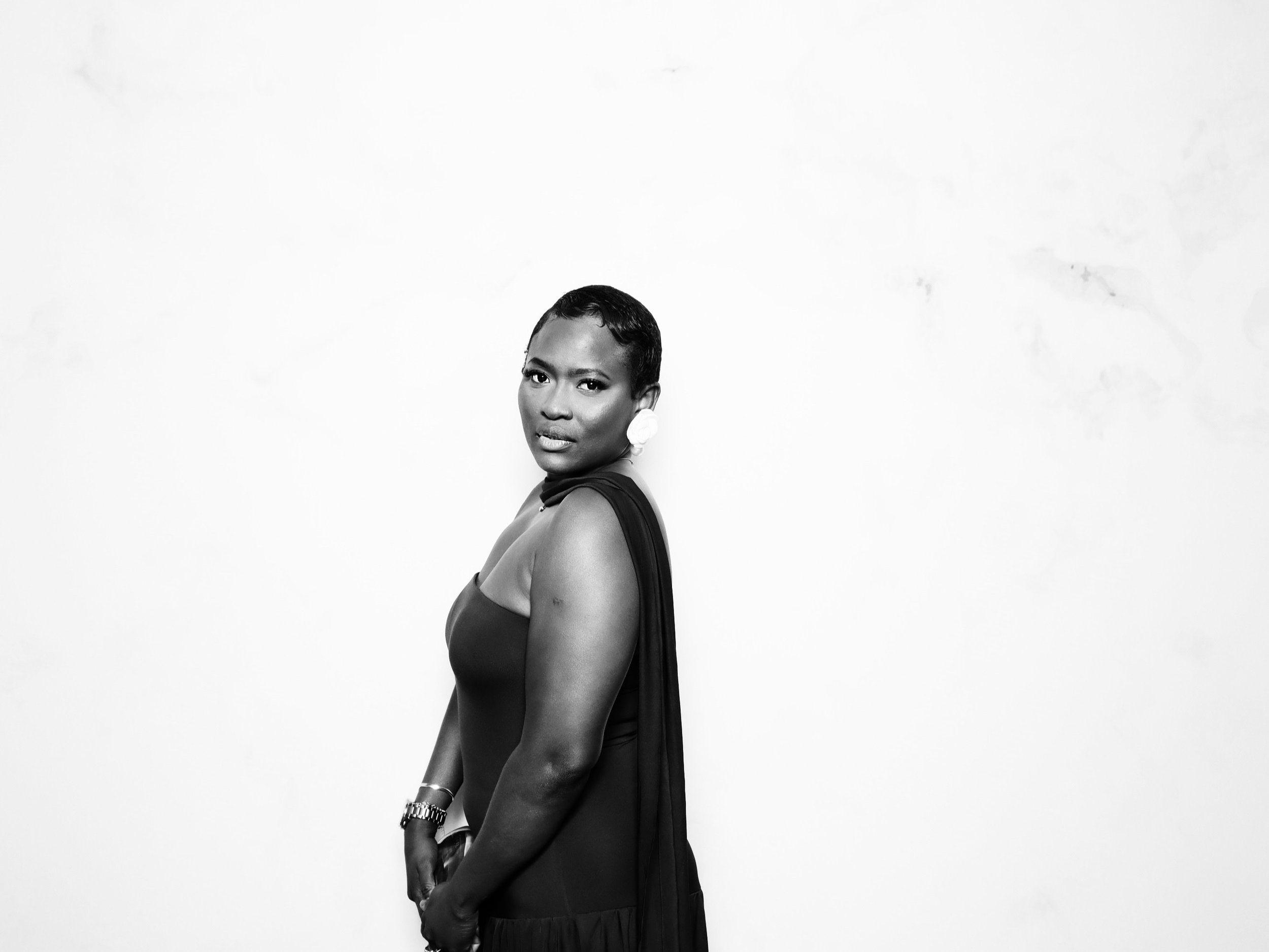 Black and white photo of a woman with short hair, wearing a sleeveless dress, looking at the camera against a plain white background.