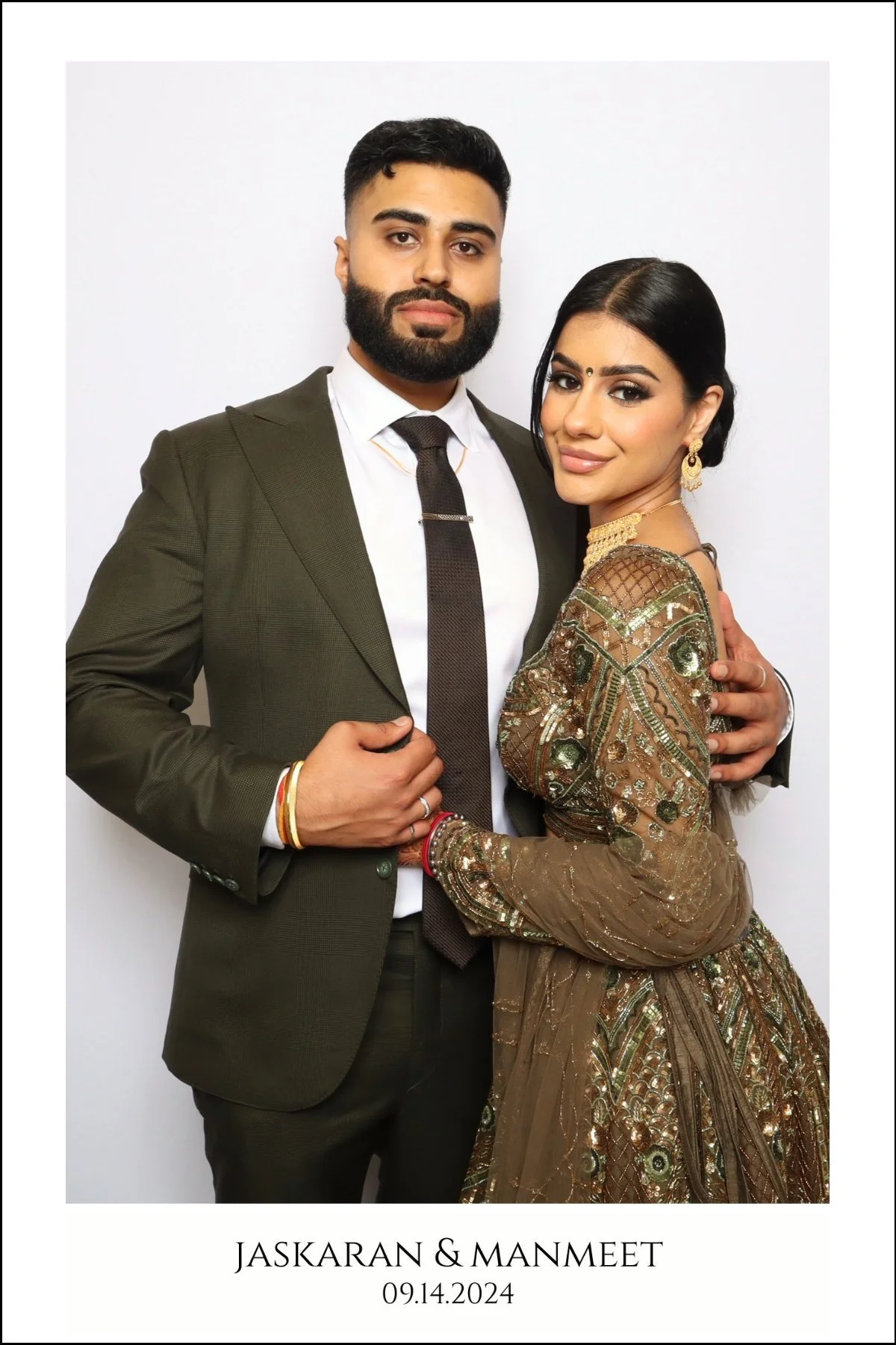 A couple dressed in formal attire, with the man in a suit and the woman in an ornate traditional dress, standing against a white background for a wedding or special event photo. The text below indicates their names, Jaskaran and Manmeet, and the date September 14, 2024.
