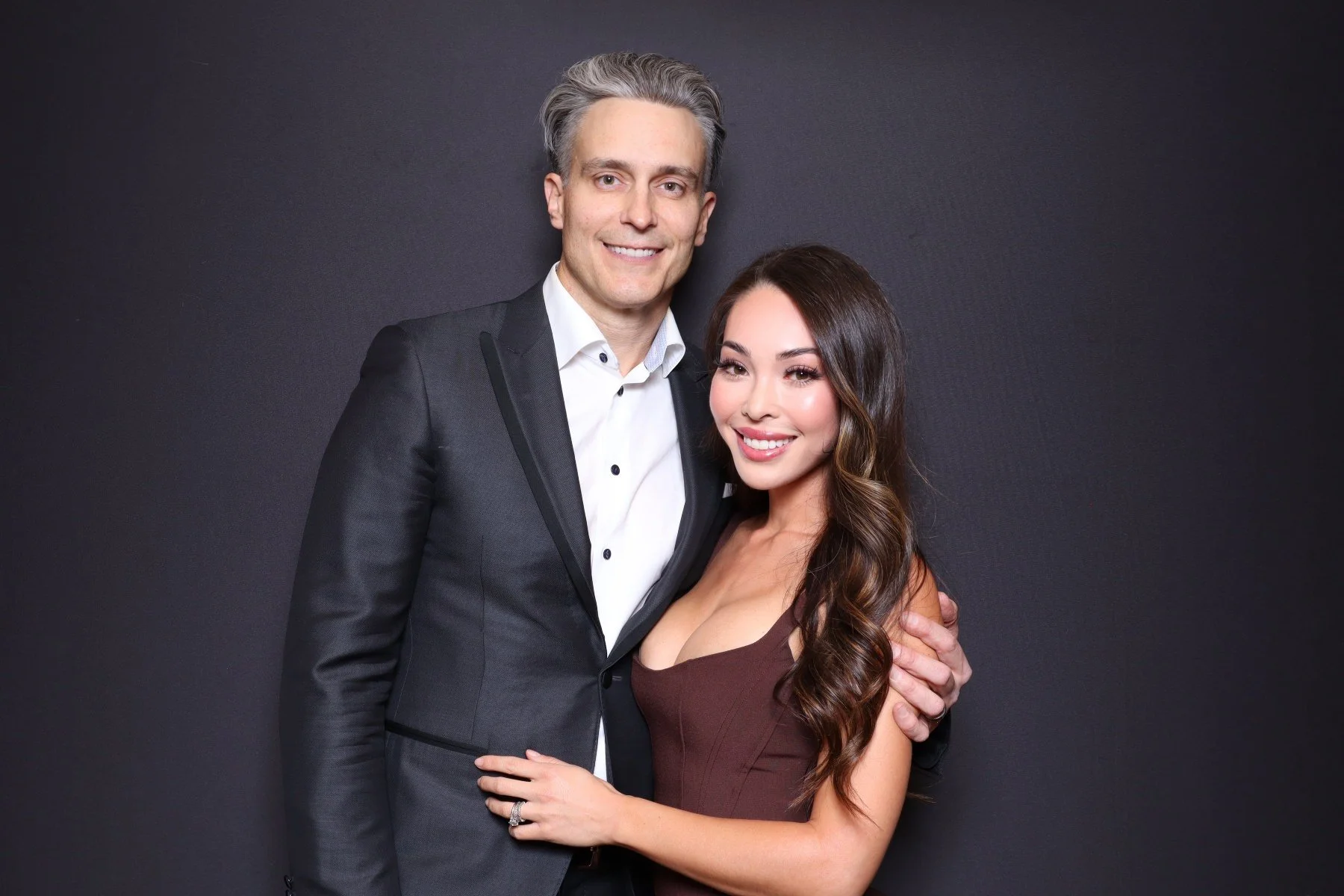 A man and woman dressed formally, smiling and posing against a dark background.