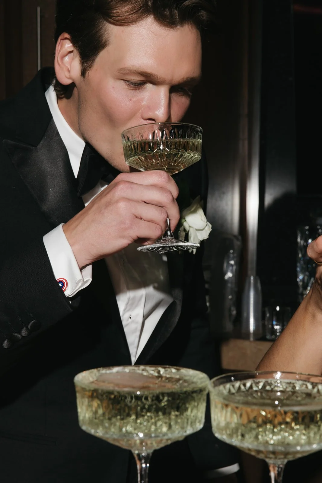 Man in a tuxedo smelling a cocktail in a coupe glass.