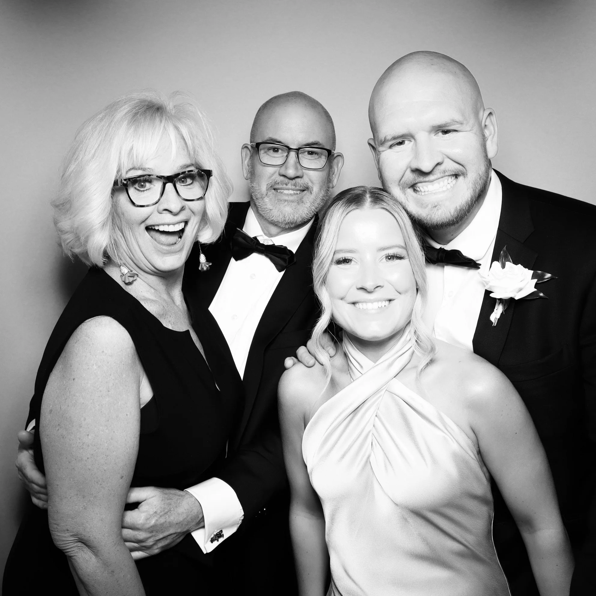 Black and white photo of four people dressed in formal attire at a celebration or wedding, smiling and posing together.