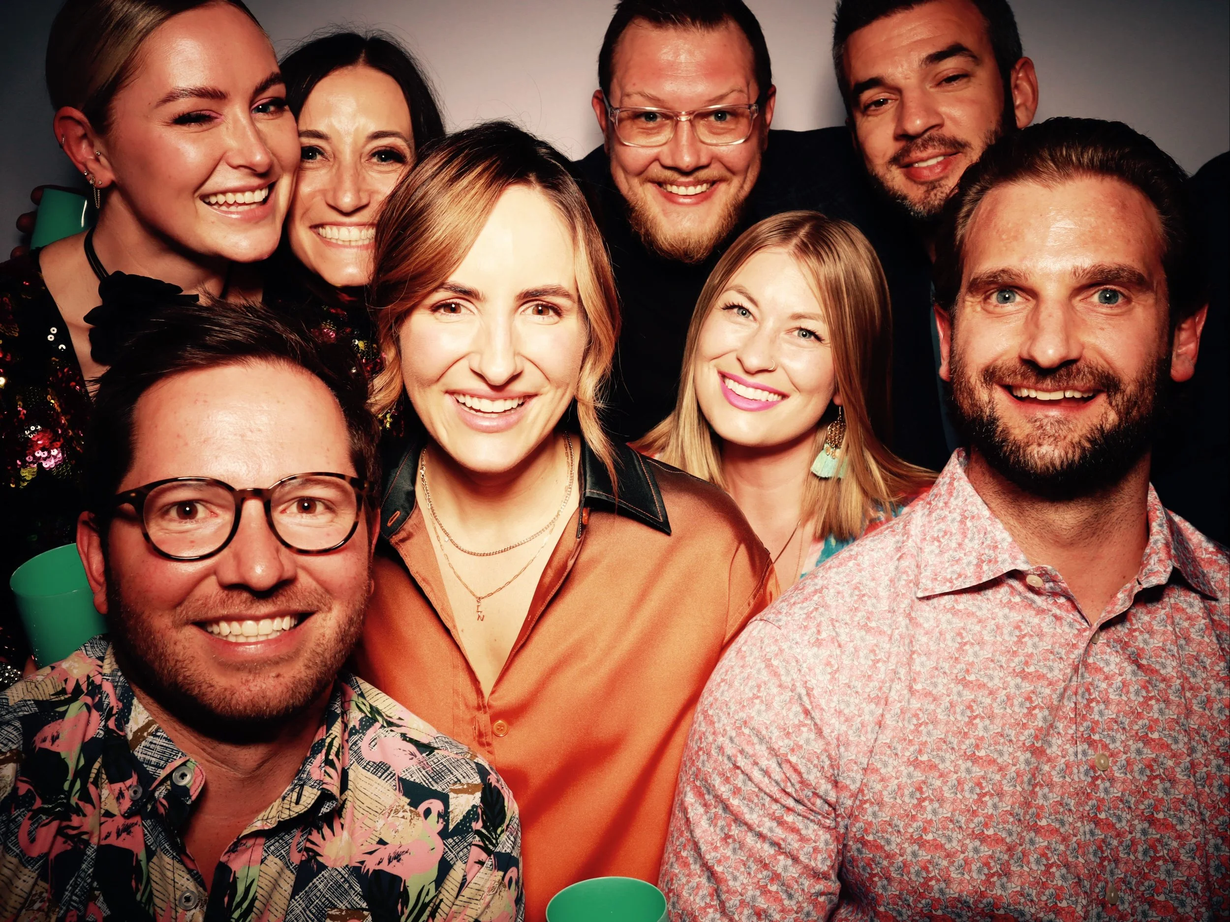 Group of nine friends smiling at a party, closely gathered together, celebrating and enjoying themselves.