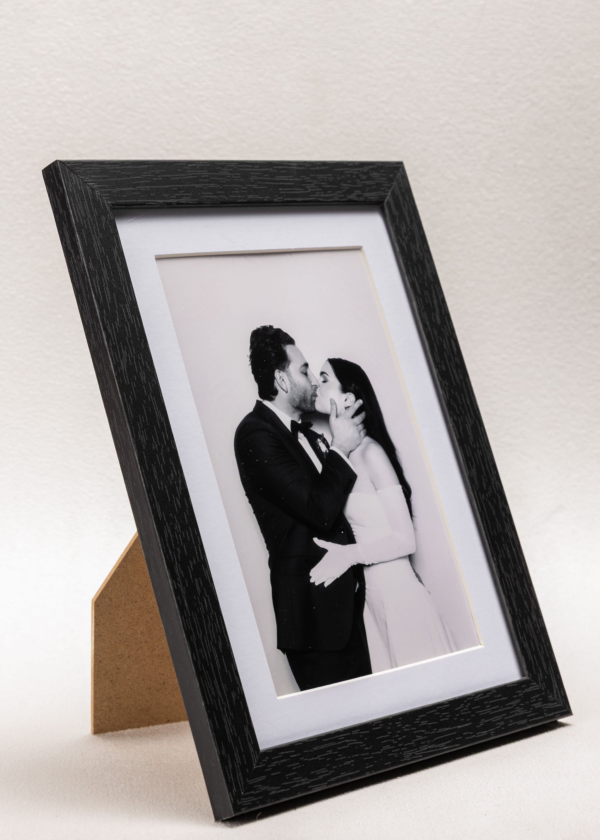 Black and white framed photograph of a couple kissing, with the man in a tuxedo and the woman in a strapless dress.