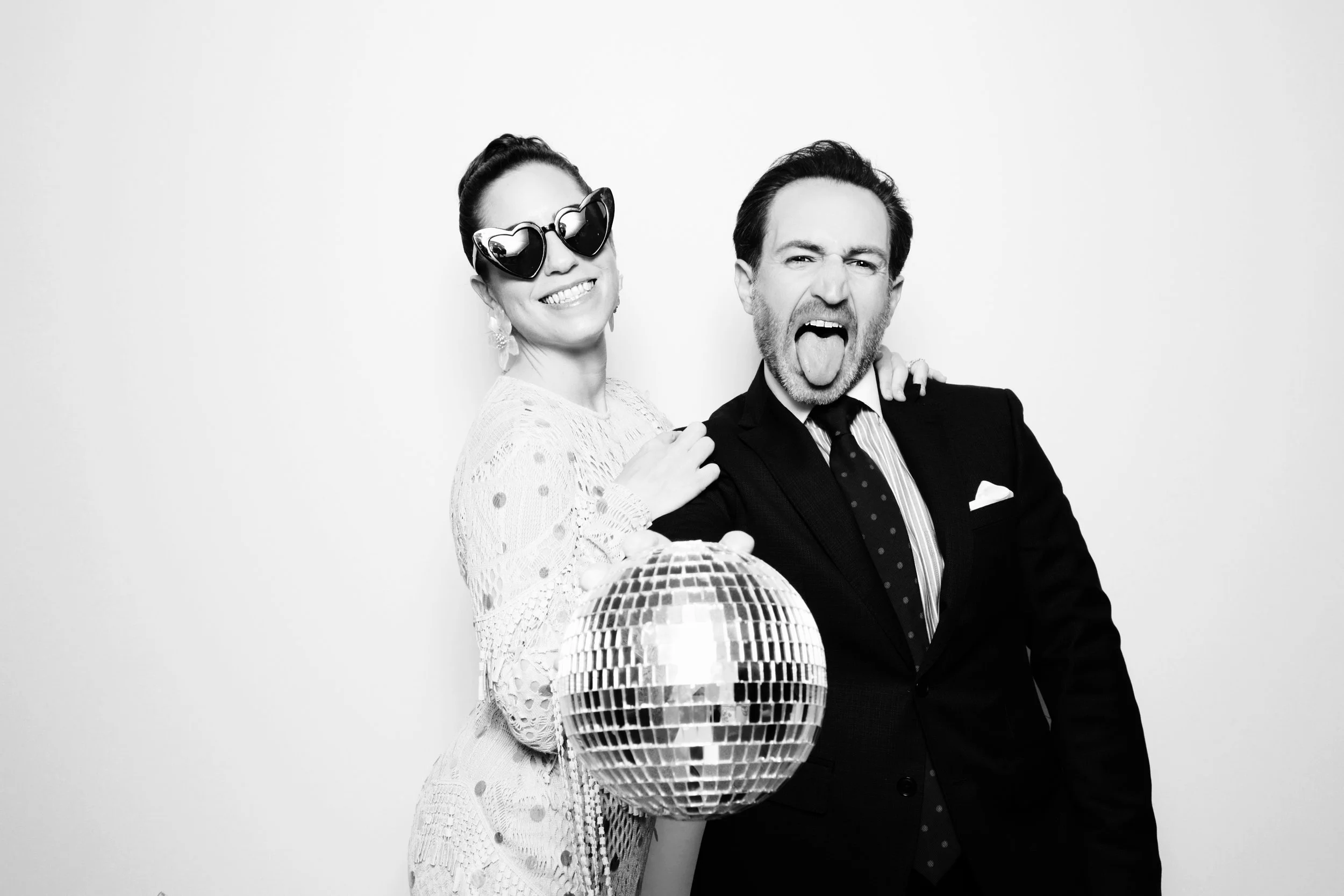 A woman in sunglasses and a woman in a suit celebrating with a disco ball.
