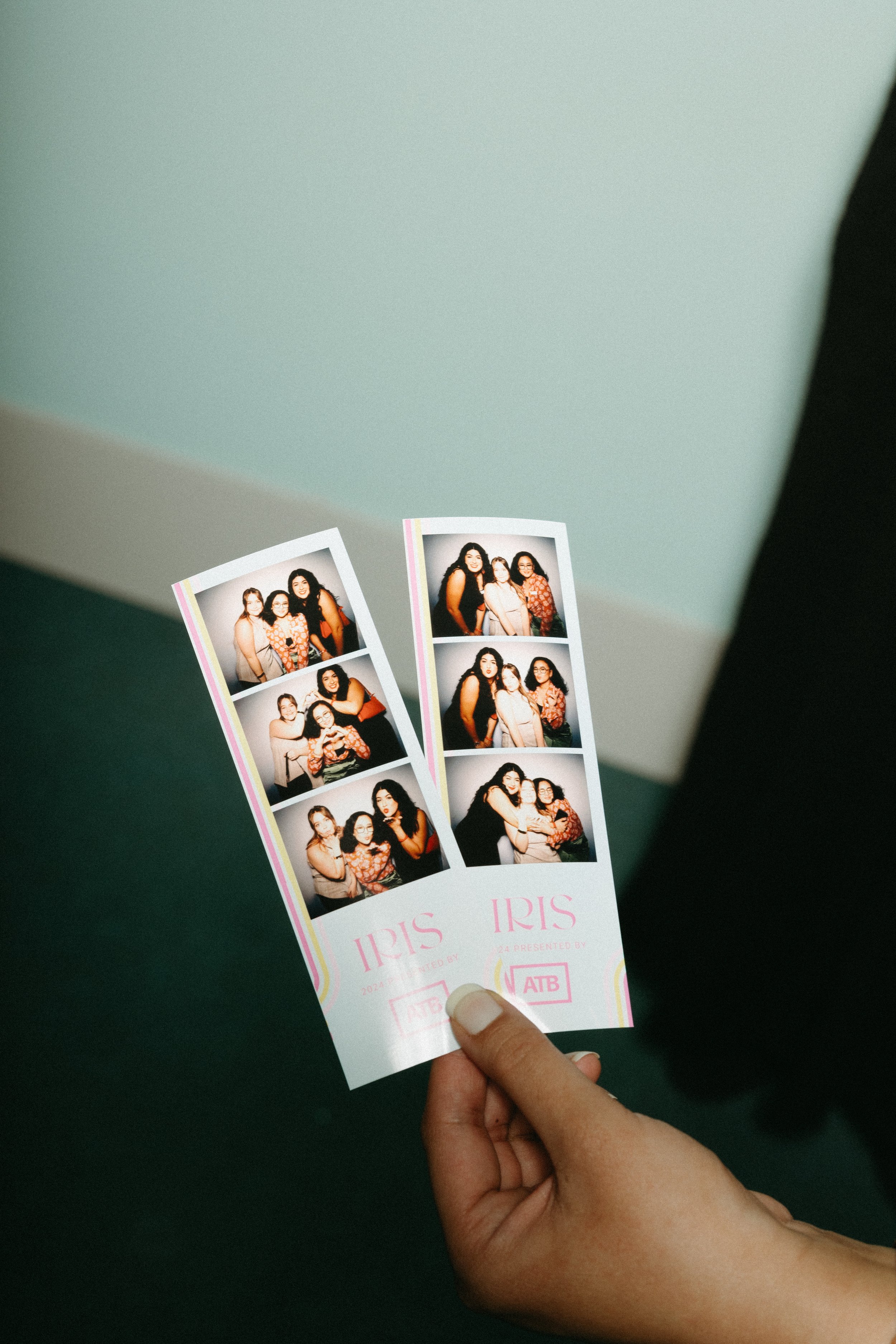 Person holding two photo booth strips with group photos against a plain background.