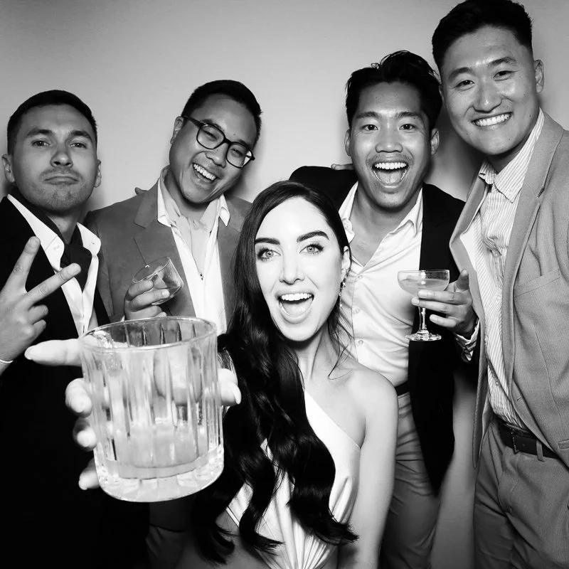 Group of five young adults celebrating, smiling, and holding drinks at a party, in black and white photo.