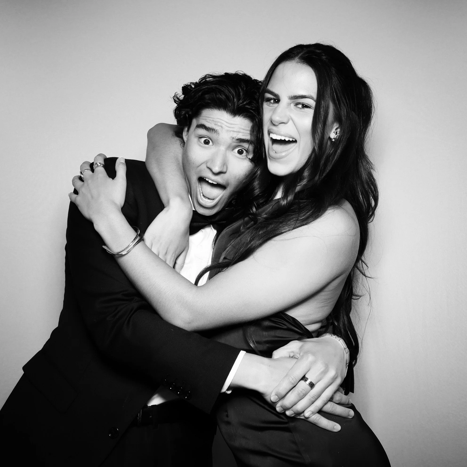 Black and white photo of a man and woman hugging and making funny faces at the camera.