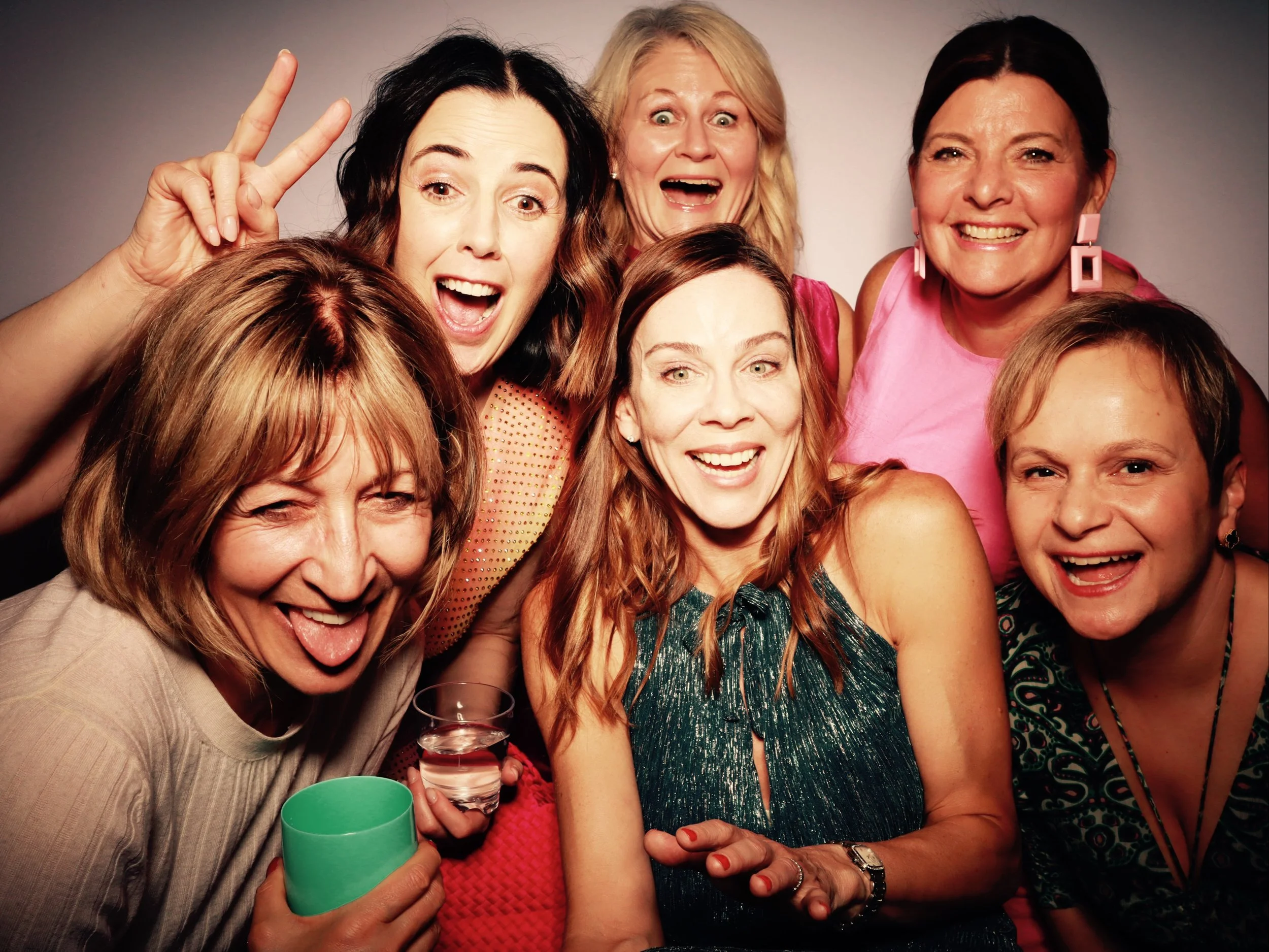 Group of seven women smiling, laughing, and showing excitement at a party or celebration.