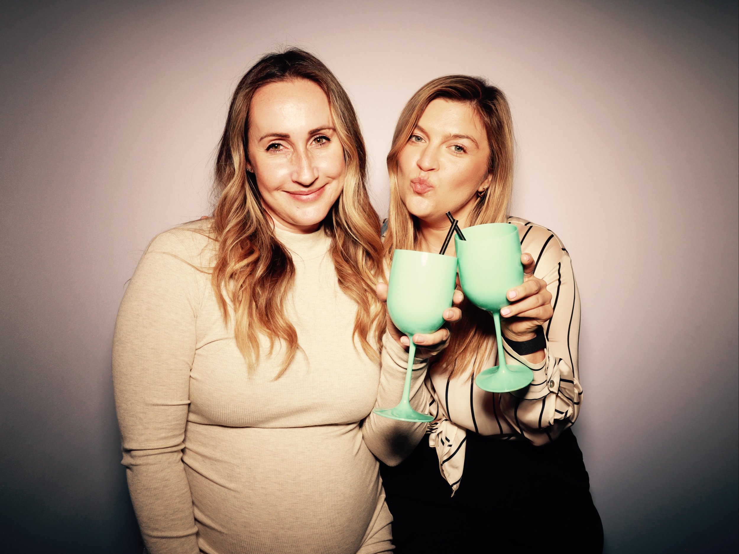 Two women smiling and holding matching green drinks with straws, celebrating together.