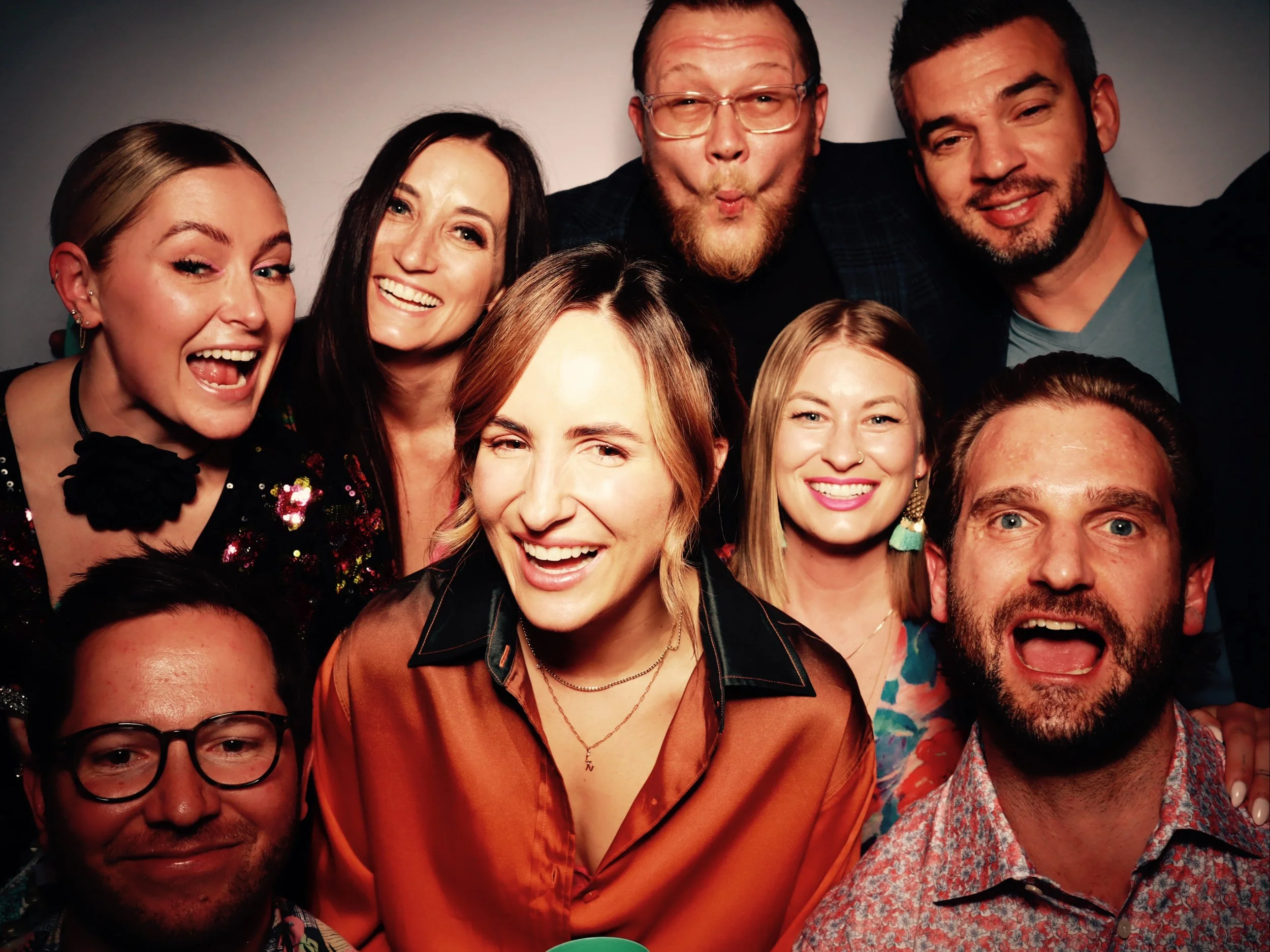 Group of nine diverse people smiling and posing closely together at a party or gathering.
