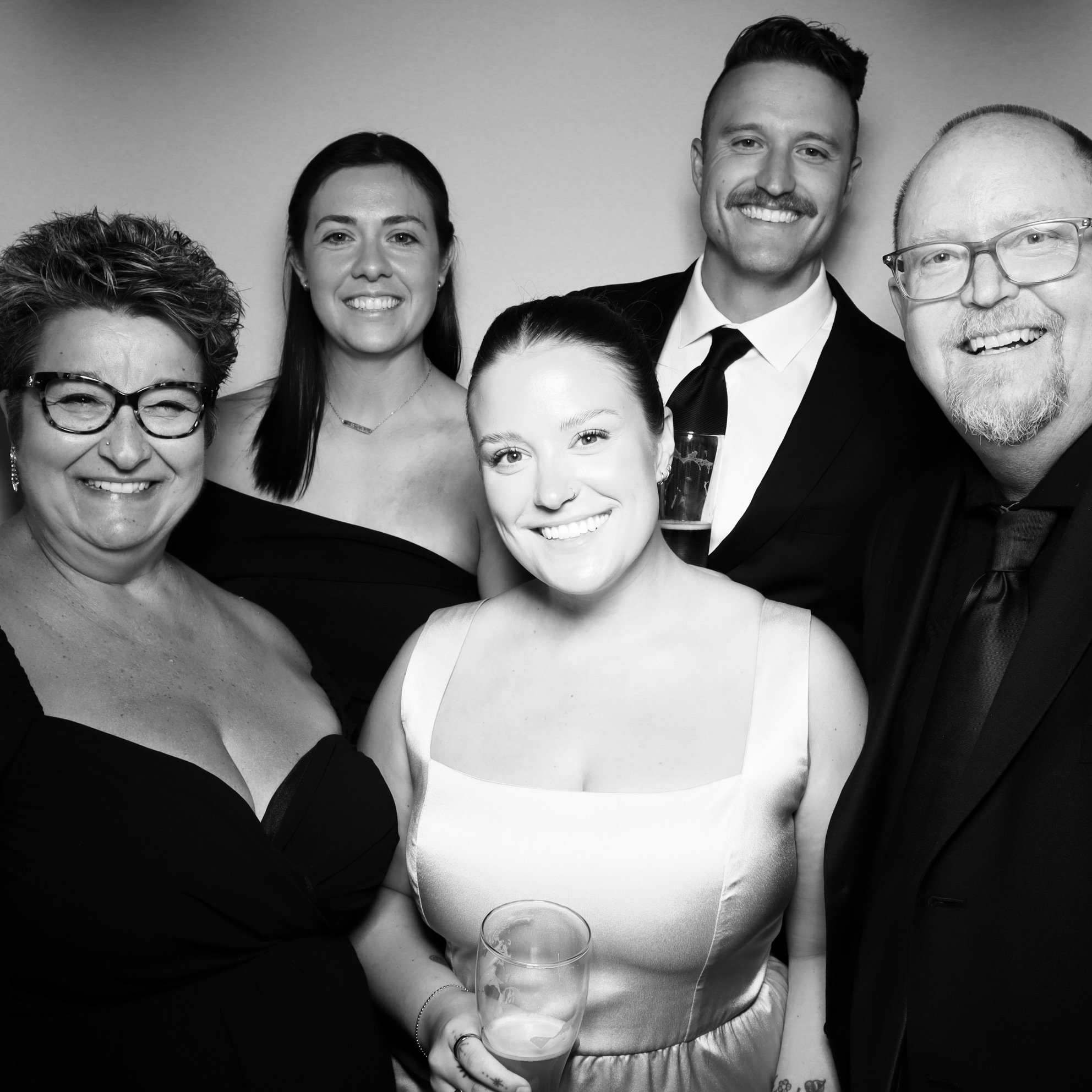 A group of six people dressed in formal attire, smiling at a party, with some holding drinks in their hands.