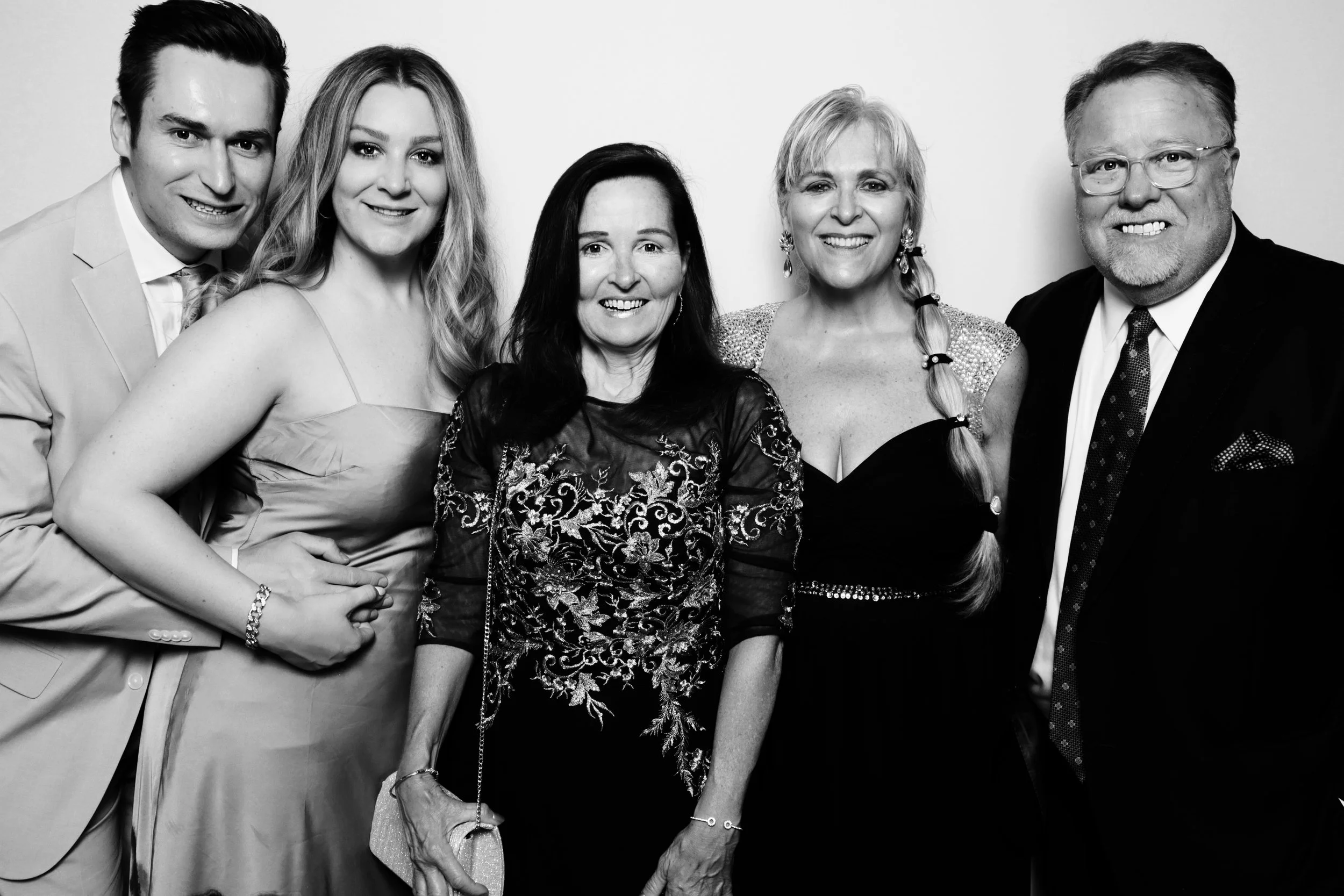 Group of five people dressed in formal attire, smiling, standing together for a photo.