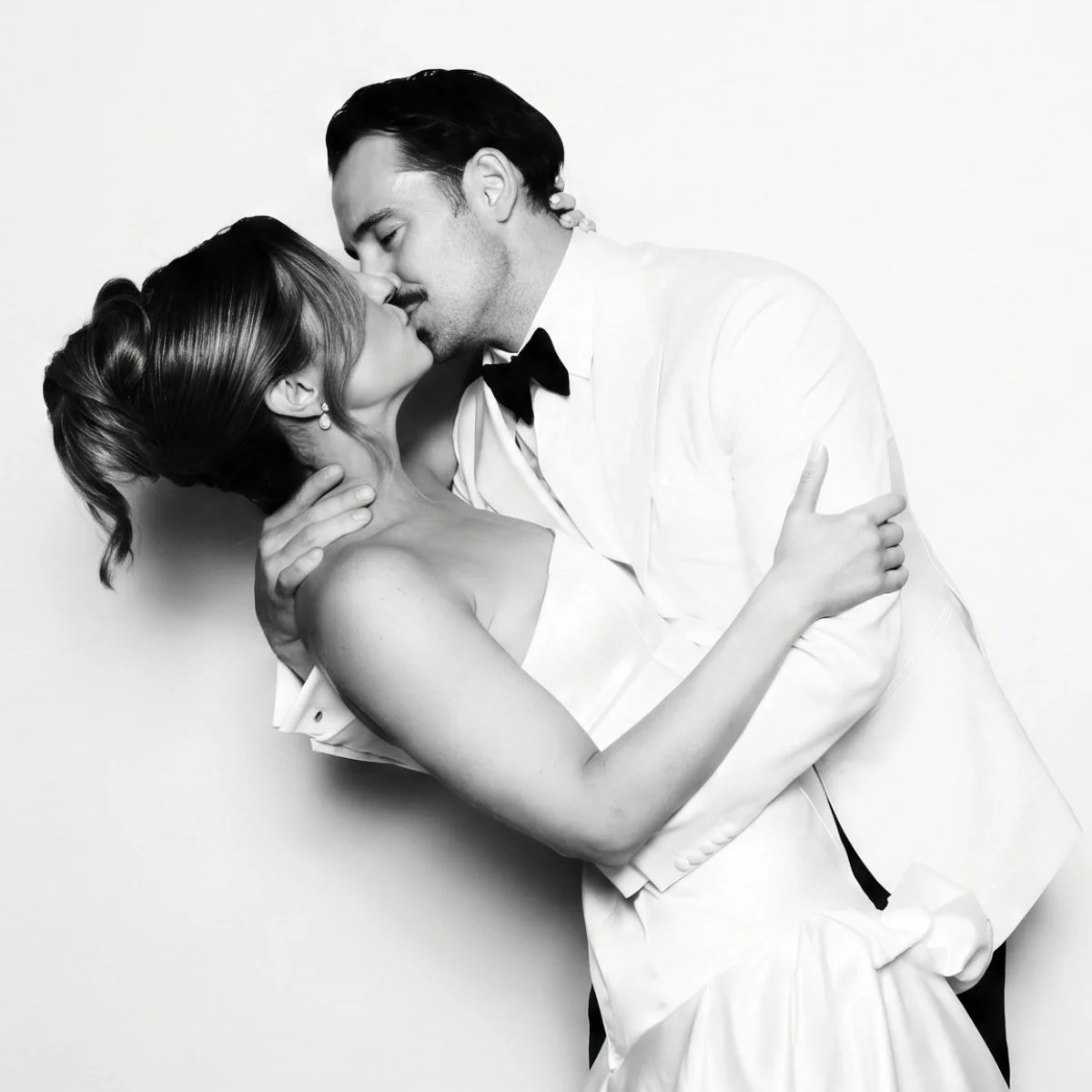 A black-and-white photo of a romantic moment between a man and woman dressed in formal attire, about to kiss.