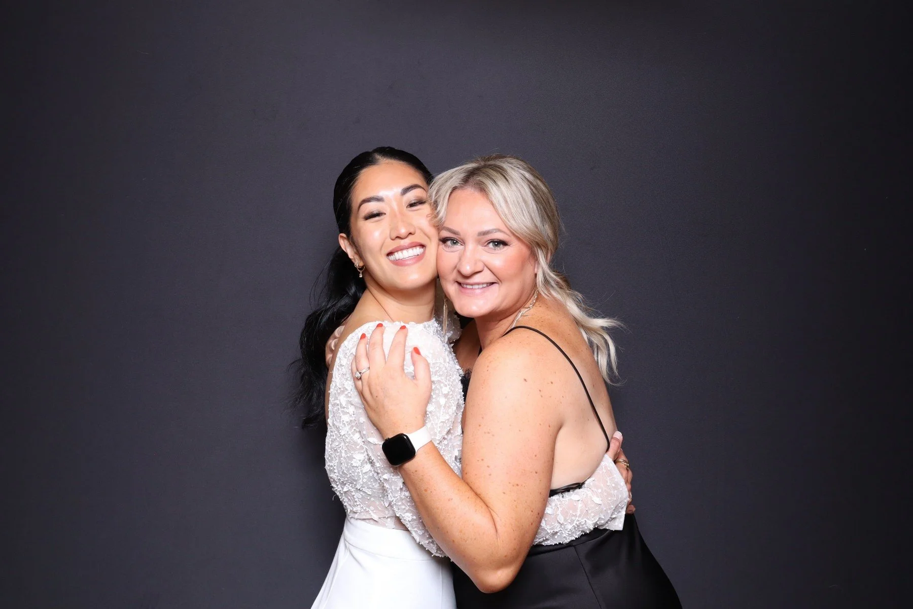 Two women hugging and smiling at the camera against a dark background.