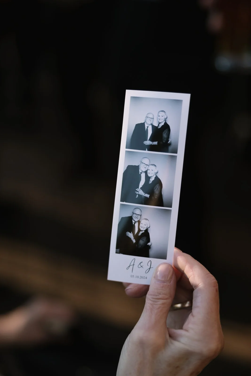 Photobooth strip with three black-and-white photos of a couple embracing, signed 'A & J' with the date '05.10.2024' at the bottom.