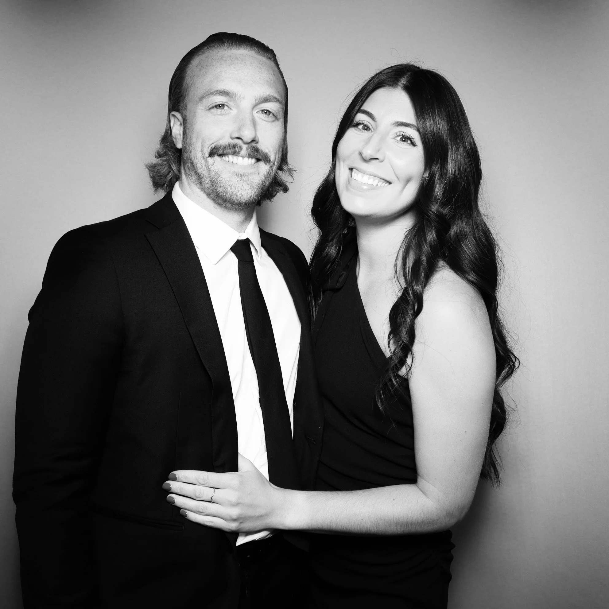 A smiling man and woman in formal attire posing together against a plain background.