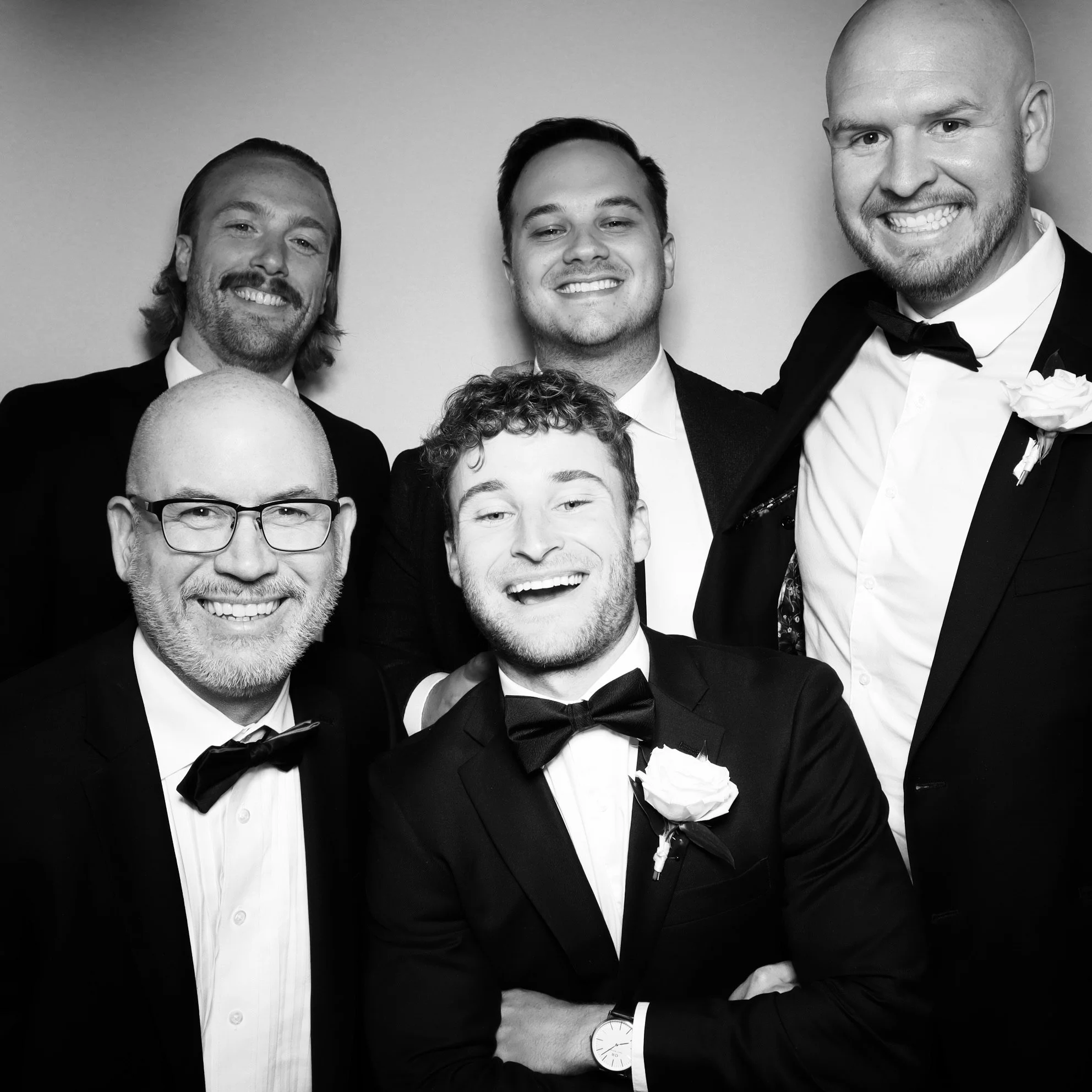 A group of six men dressed in tuxedos, smiling for a photo in black and white.