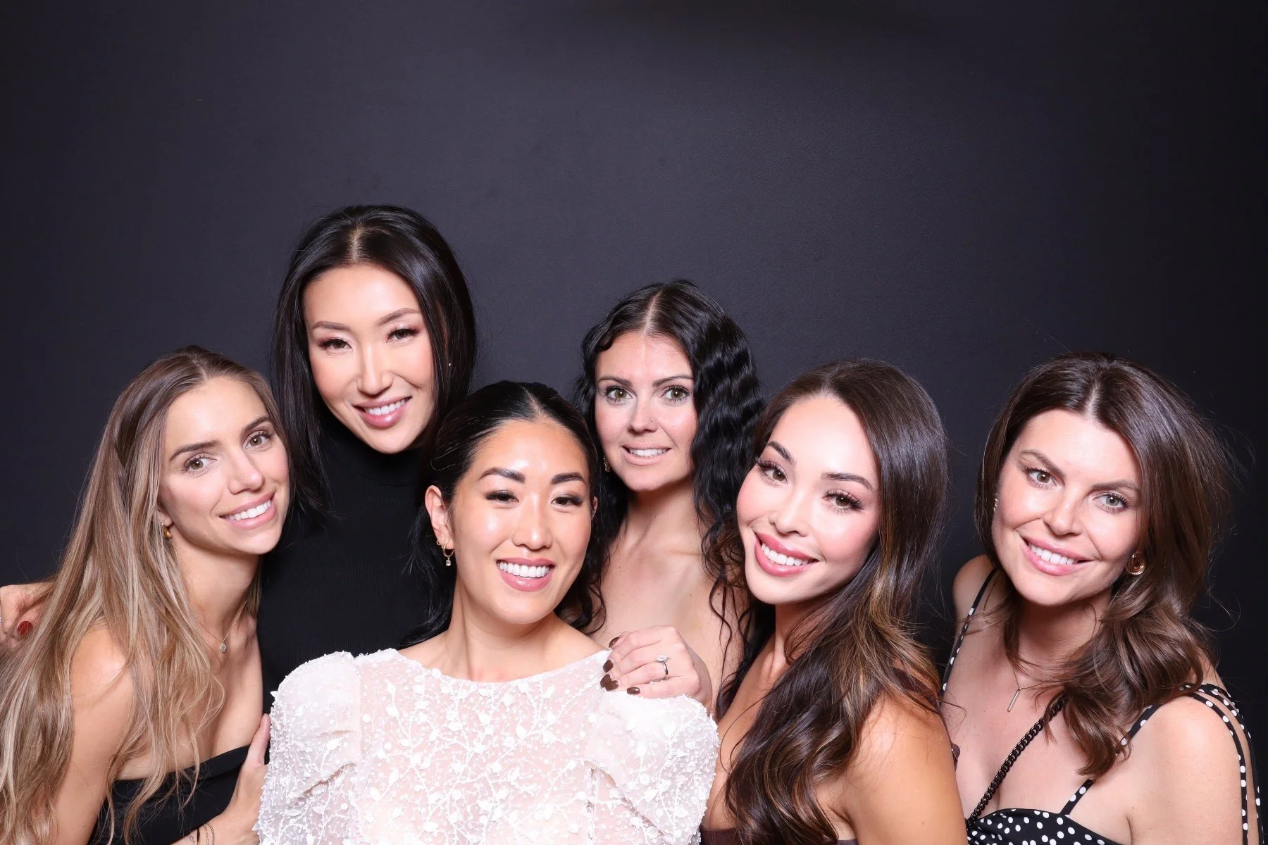 Group of six women smiling and posing against a black background.