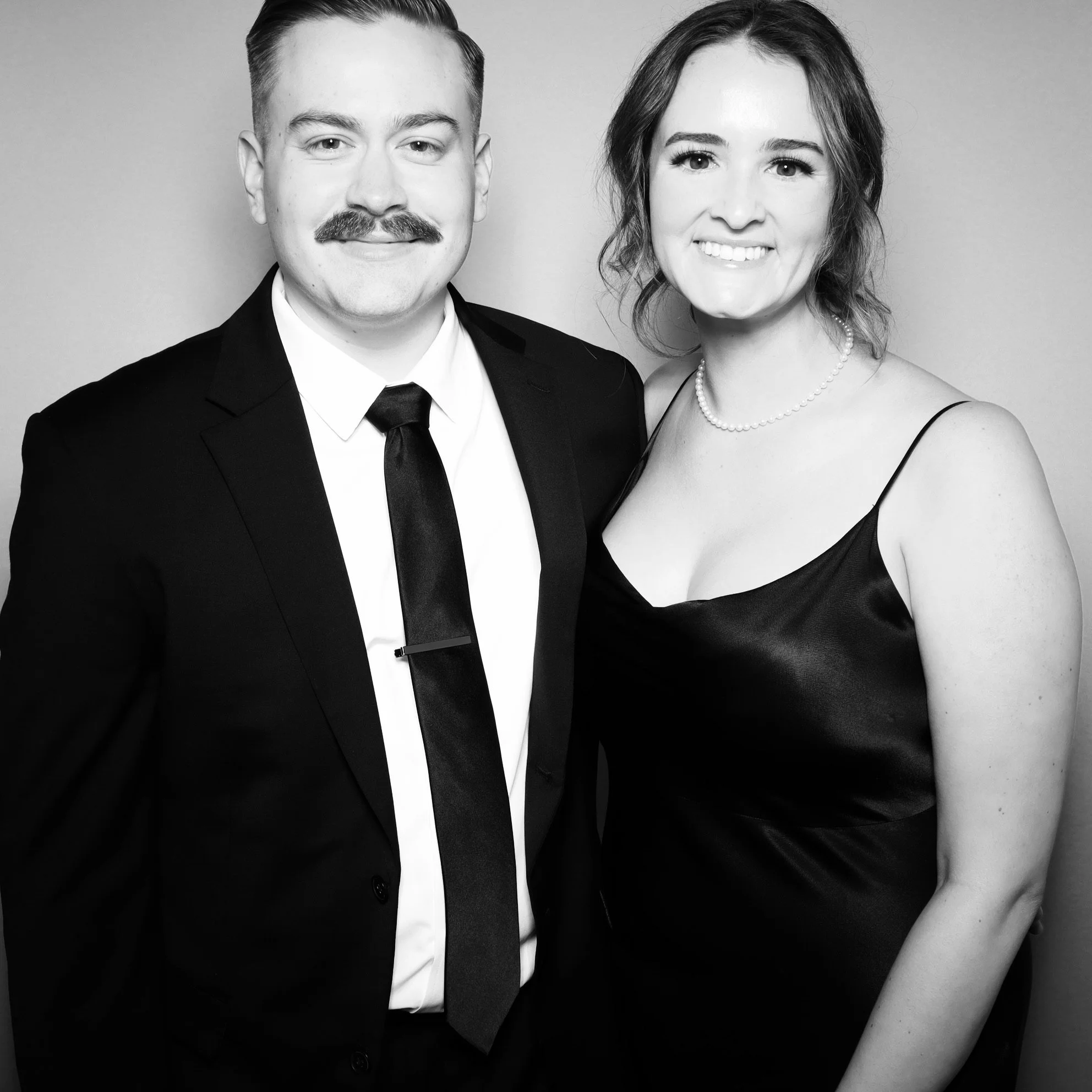 A man and woman dressed in formal attire, standing close together, smiling, in a black and white photo.