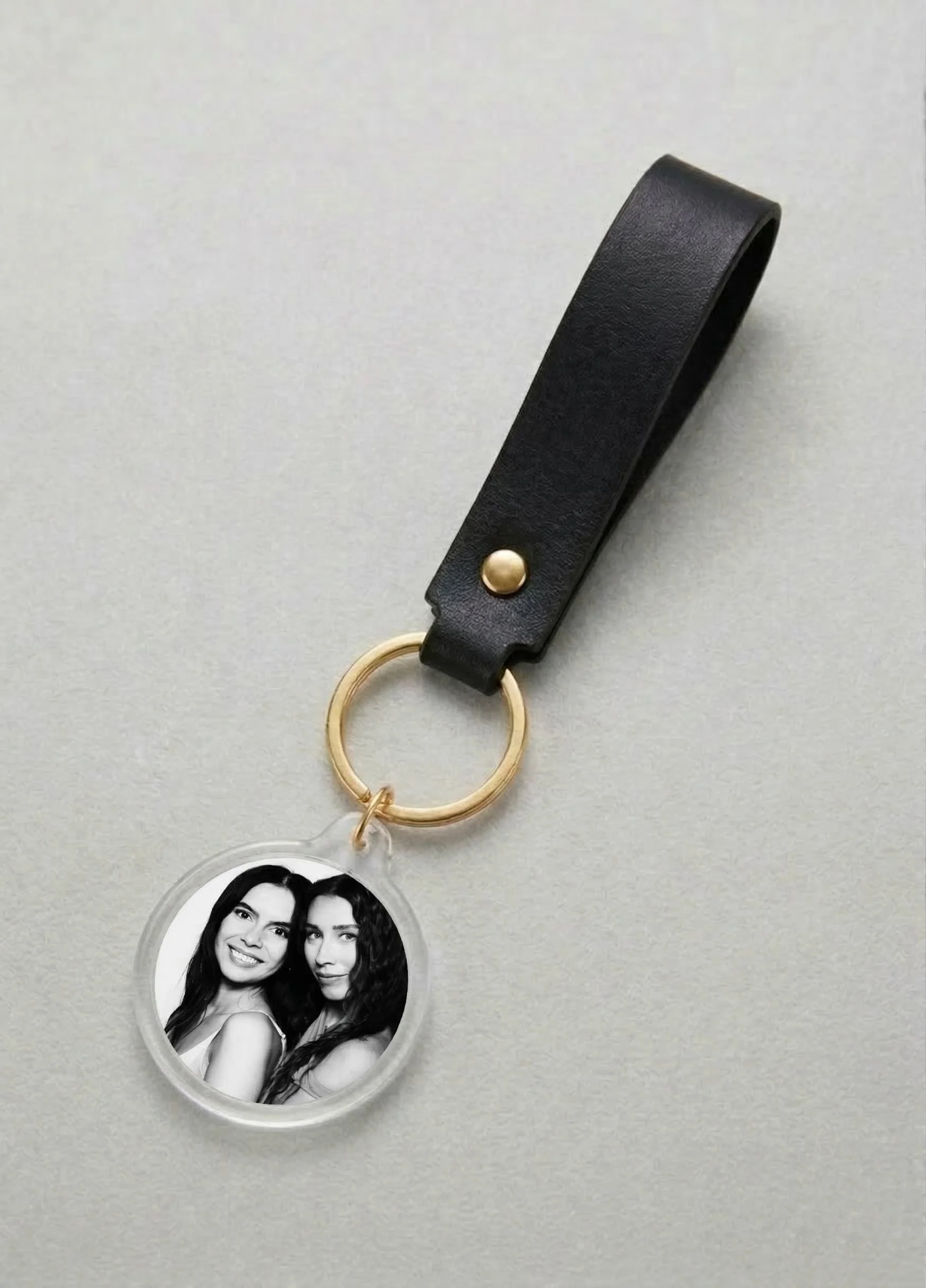 Black leather keychain with a gold ring holding a black-and-white photo of two women smiling and posing closely.