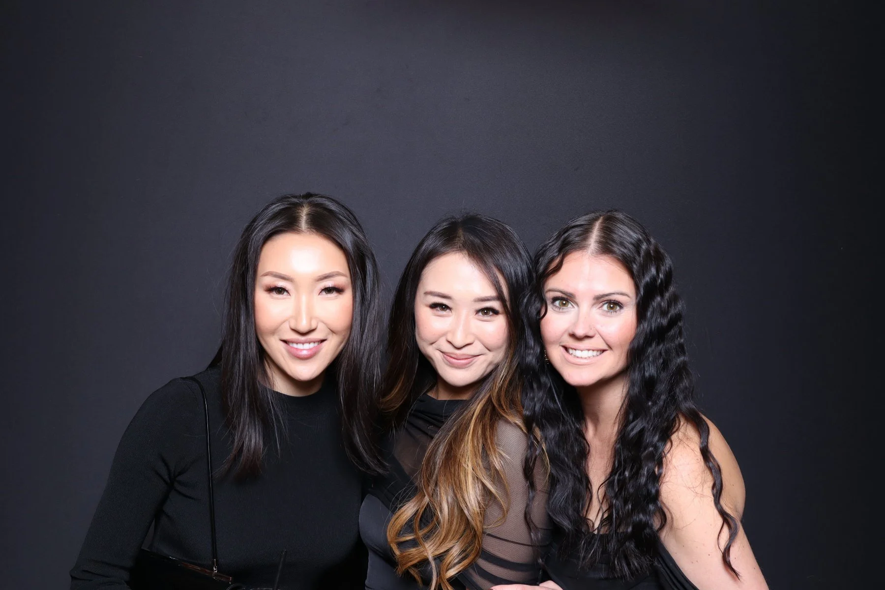 Three women smiling and posing together in front of a dark background.