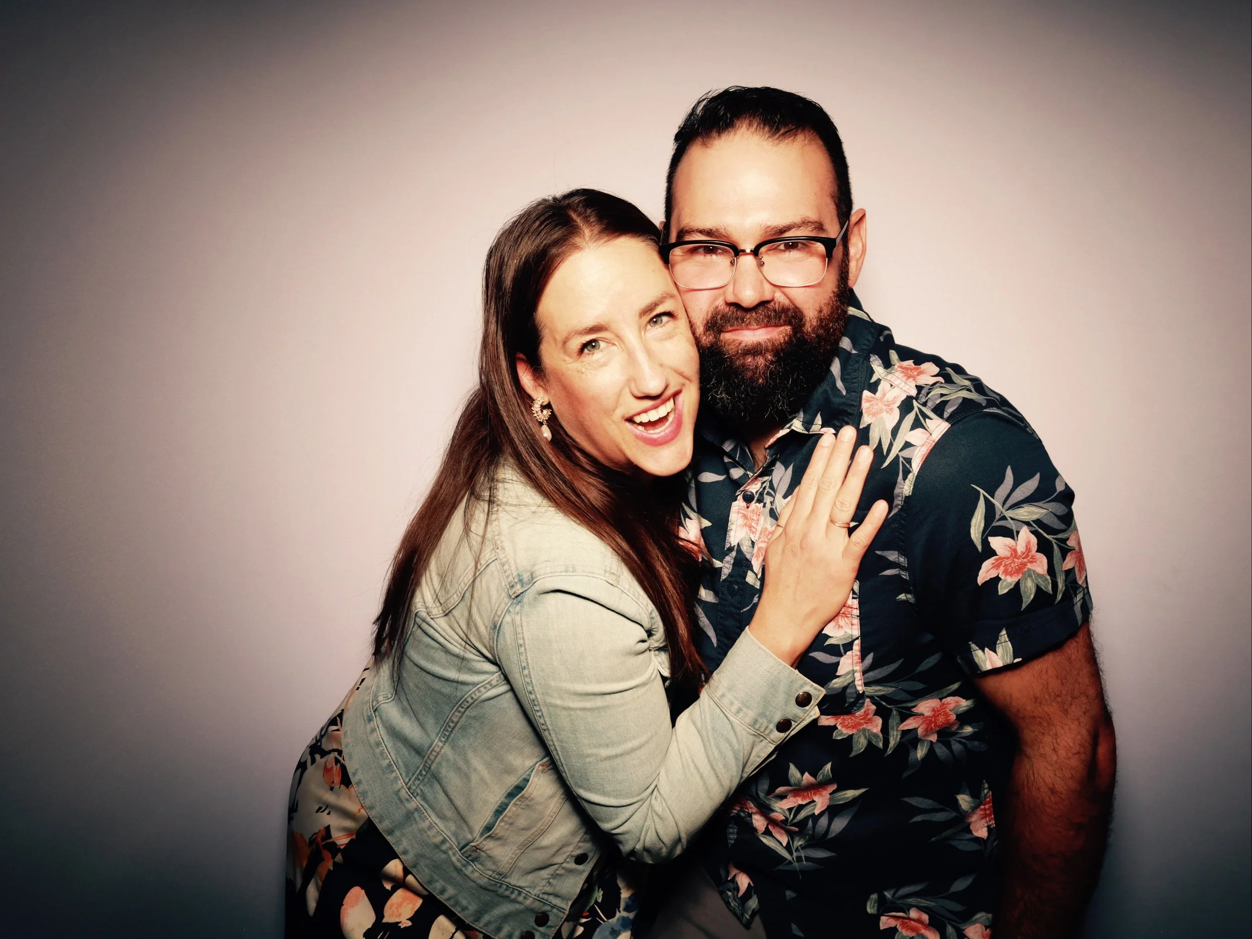 A woman and man posing closely together, smiling and showing affection, against a plain light background.