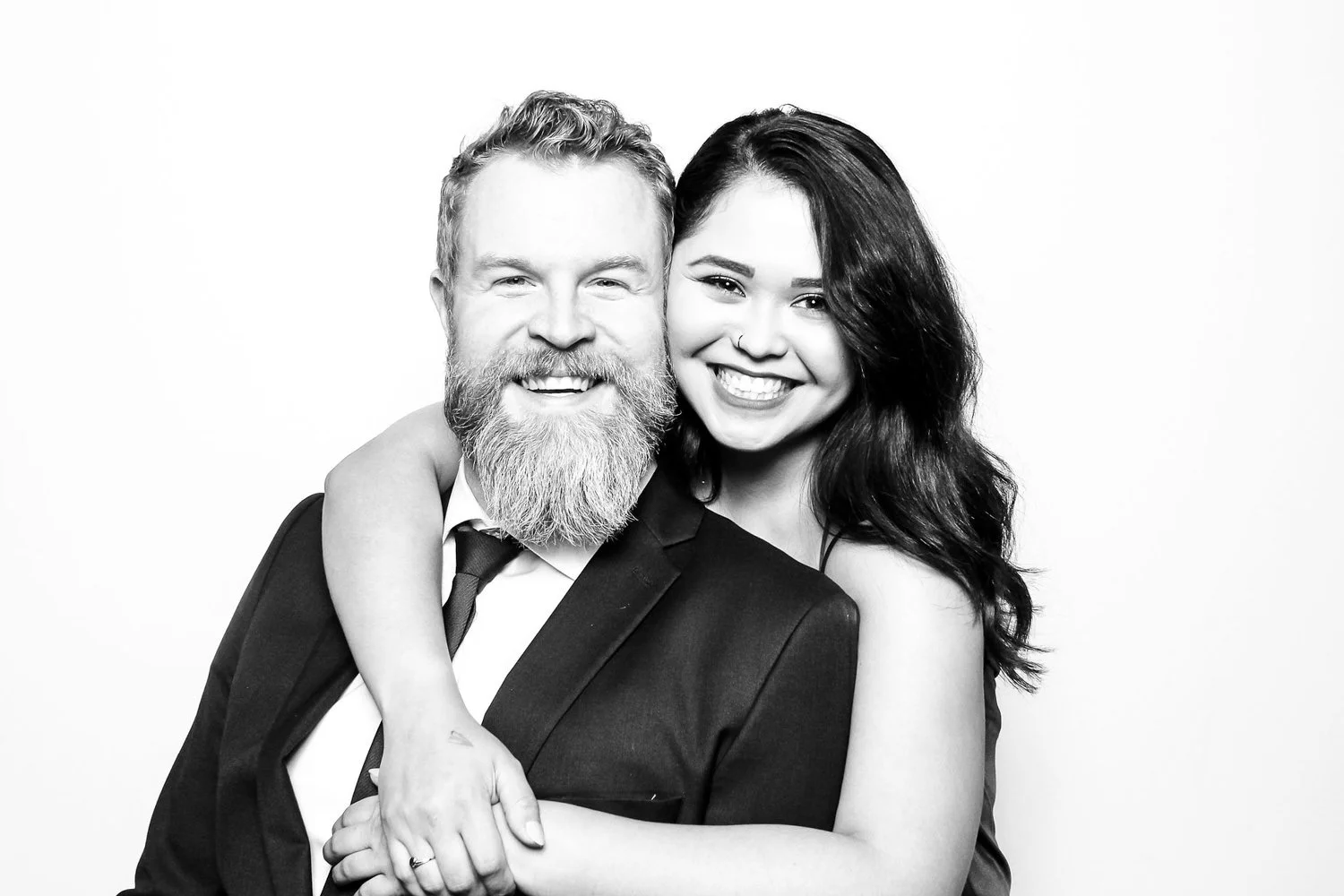 A black and white photo of a smiling man with a beard and a woman with long dark hair, embracing and showing happiness.