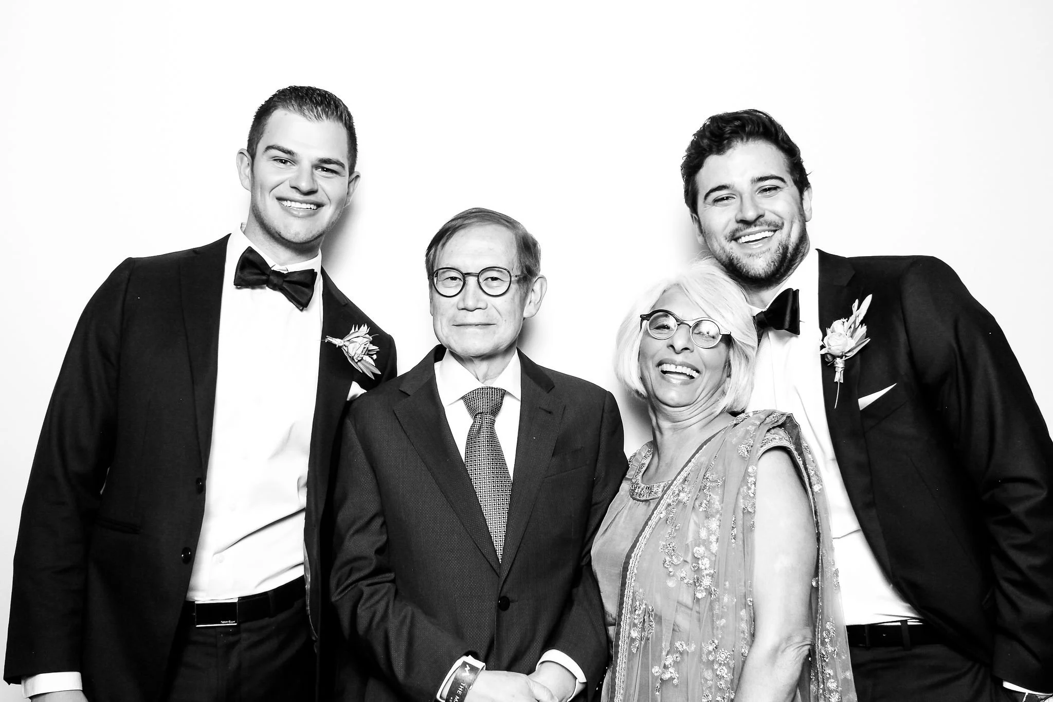 Group of four people dressed in formal attire, smiling for a photo against a white background.