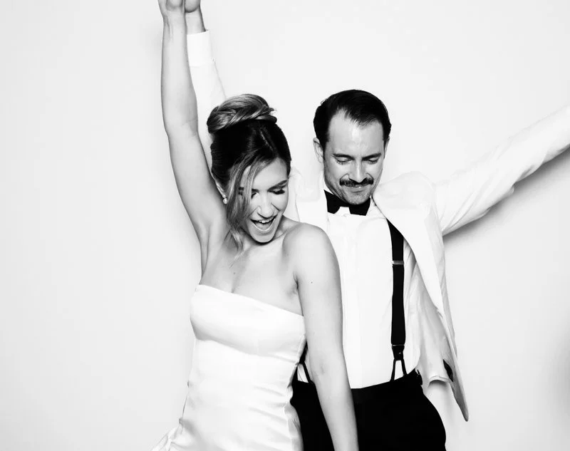 A woman in a strapless dress and a man in a tuxedo with suspenders are dancing together, smiling and enjoying themselves.