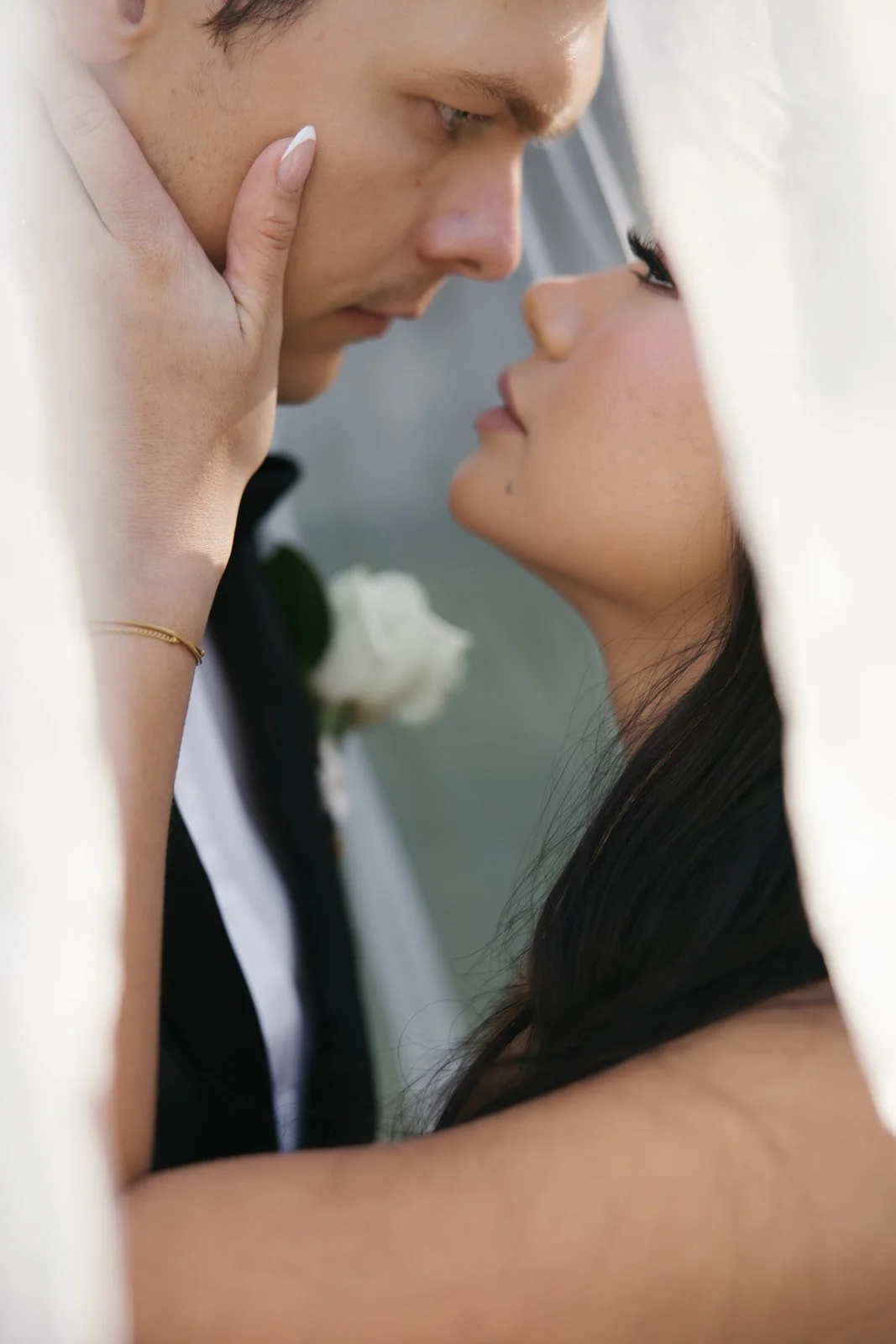 Close-up of a couple gazing into each other's eyes, with their faces nearly touching, framed by a white curtain.