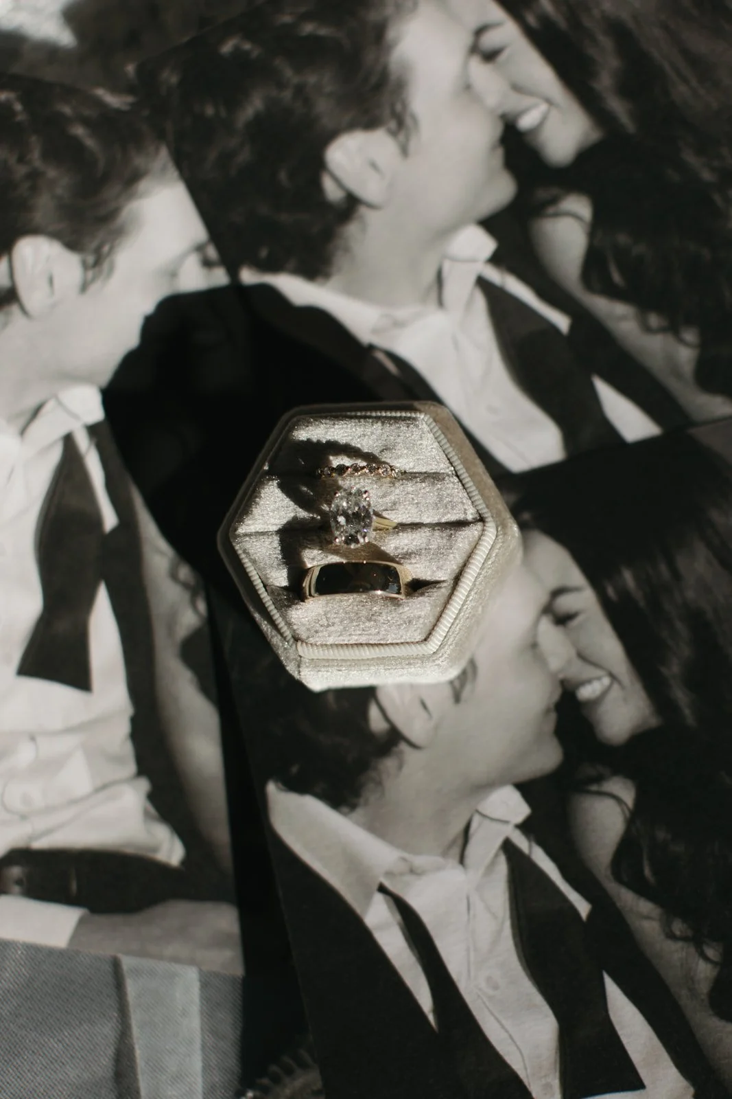 Close-up of a jewelry box with a diamond ring and bracelet inside, placed on a black-and-white photograph of two people smiling and leaning close to each other.