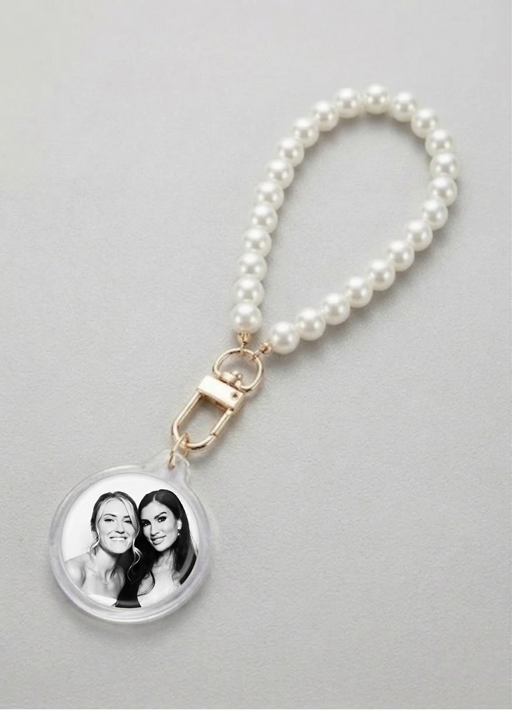 A pearl necklace with a gold clasp, attached to a circular photo holder with a black and white picture of two women smiling.