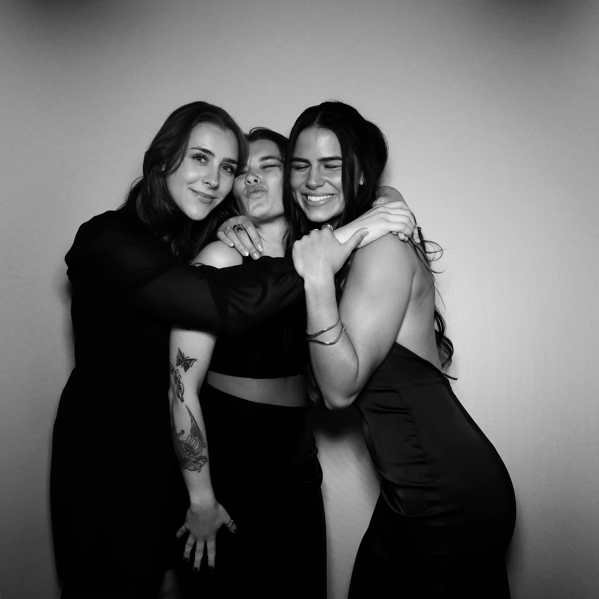 Three women hugging and smiling together in a black and white photo.