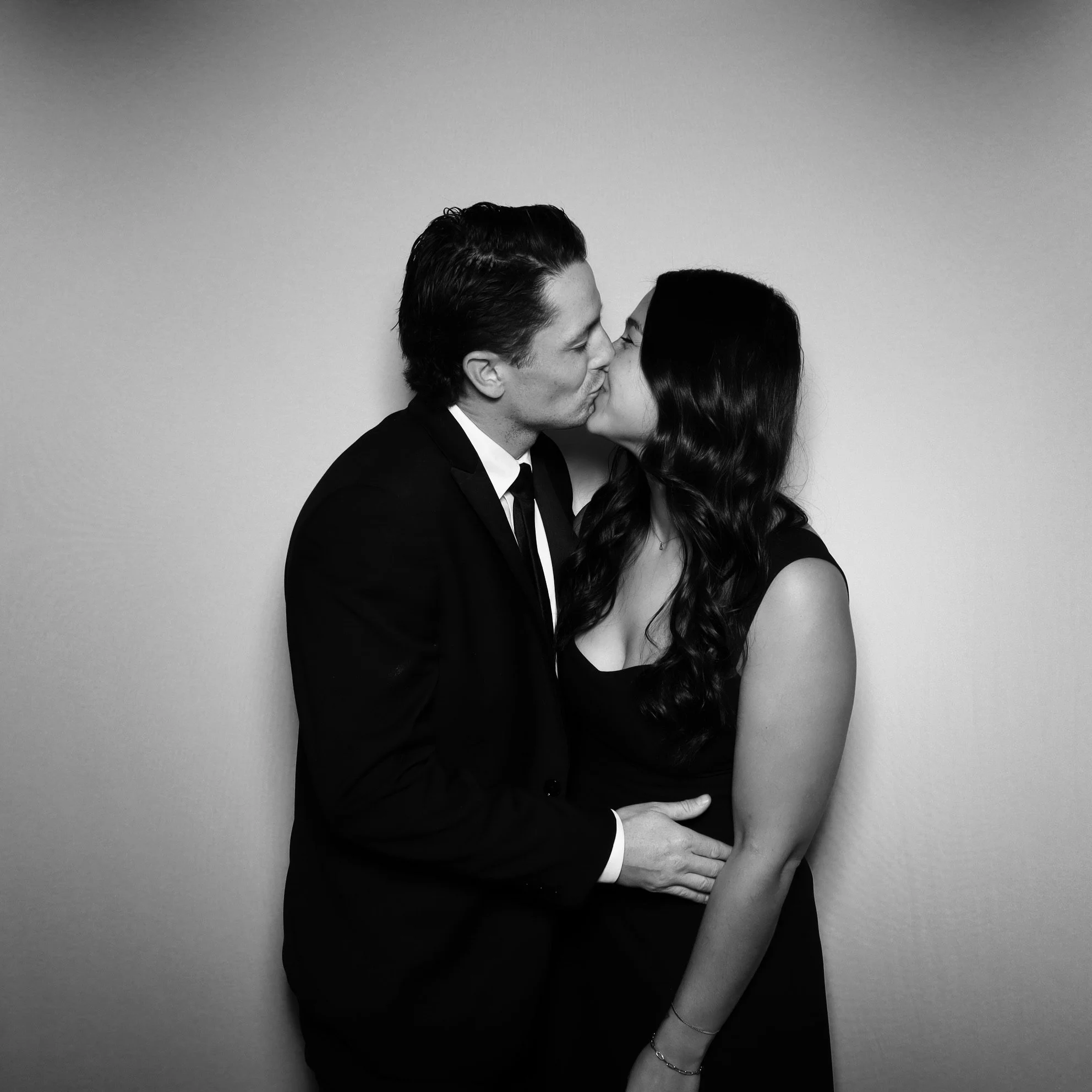 A black and white photo of a man in a suit and woman in a dress sharing a kiss.