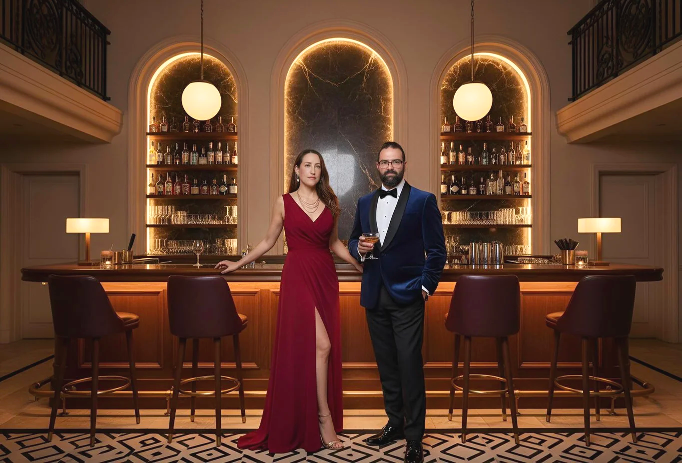 A man and woman dressed in formal attire standing at a bar in a luxurious, elegant setting with warm lighting, bottles on shelves, and a geometric patterned floor.