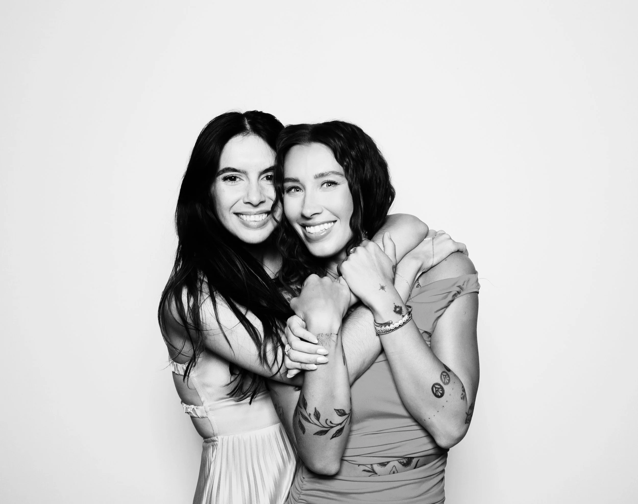 Two women hugging and smiling at the camera in a black and white photograph.