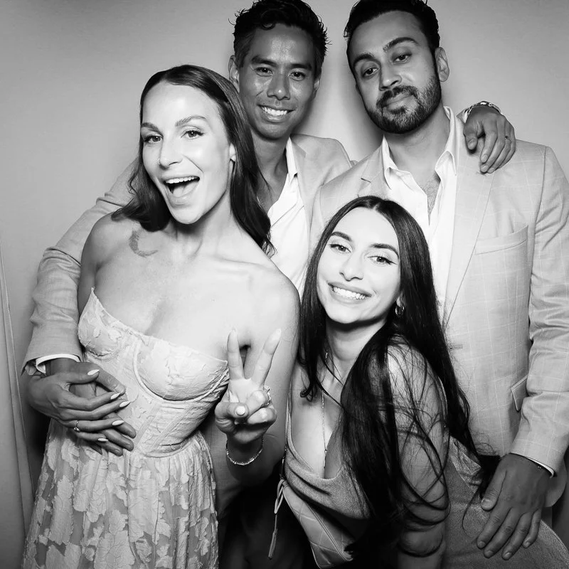 Black and white photo of four diverse young adults smiling and posing together, with two women and two men, in formal attire.