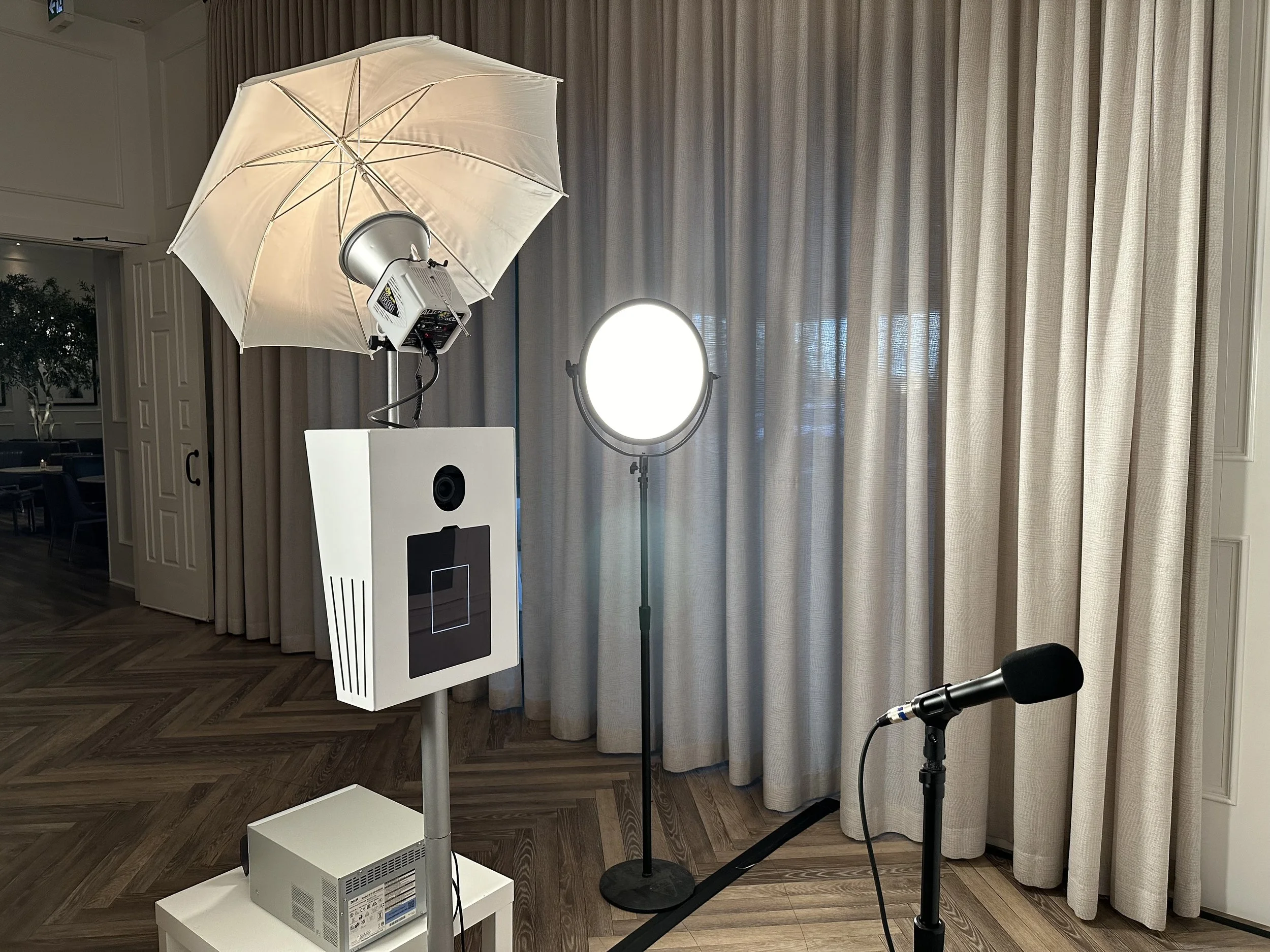 Photo of a photo booth setup with lighting equipment, a microphone, and a backdrop with curtains.