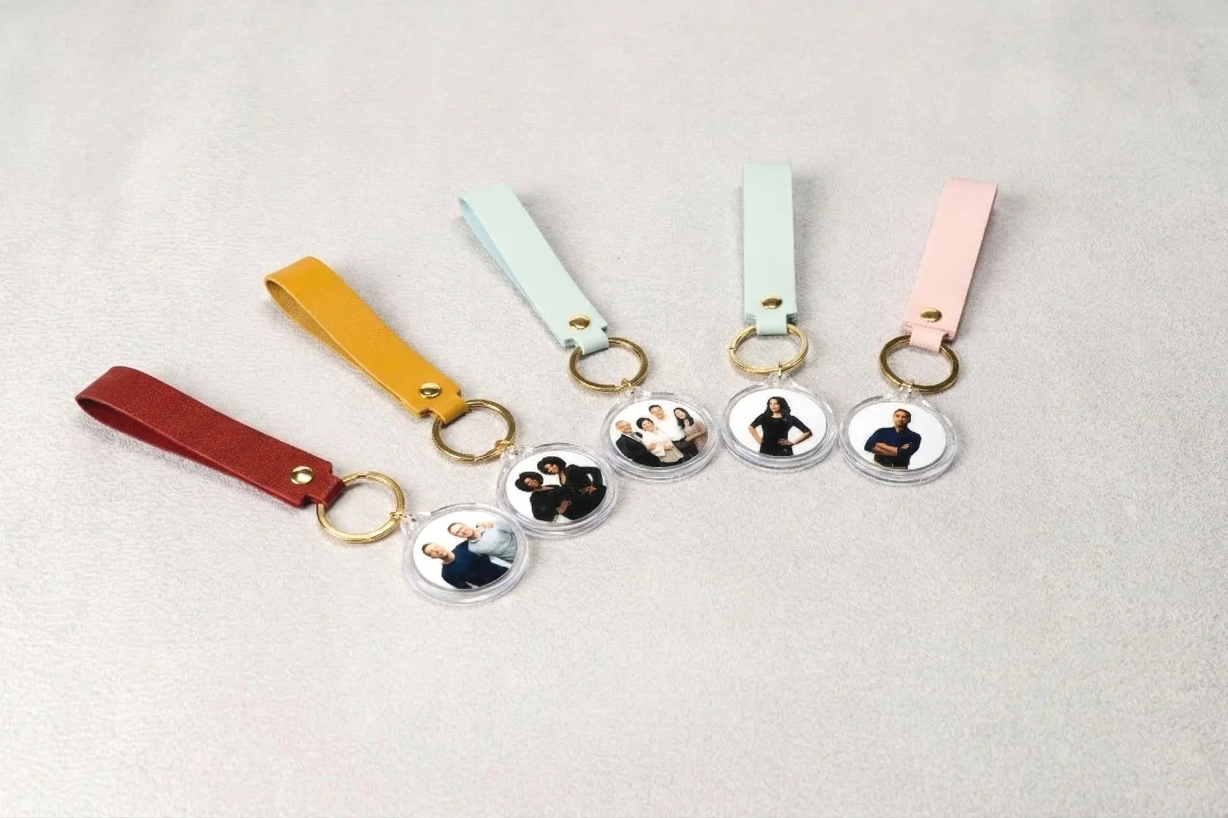 Colorful keychains with leather straps and round photo charms showing groups of people.