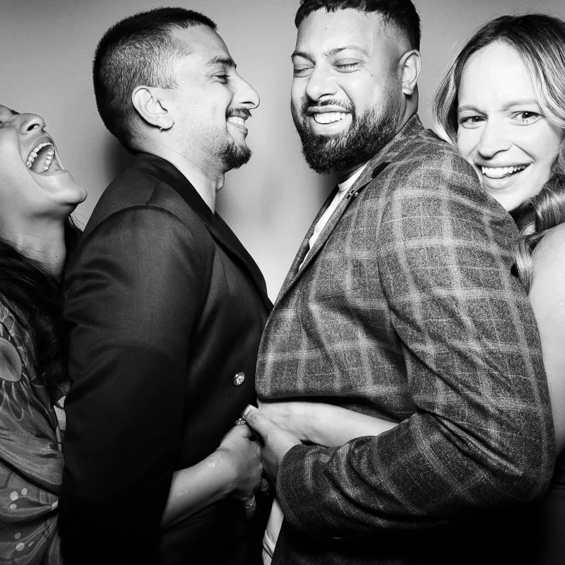 Four diverse friends in formal attire smiling and laughing together in a black-and-white photo.