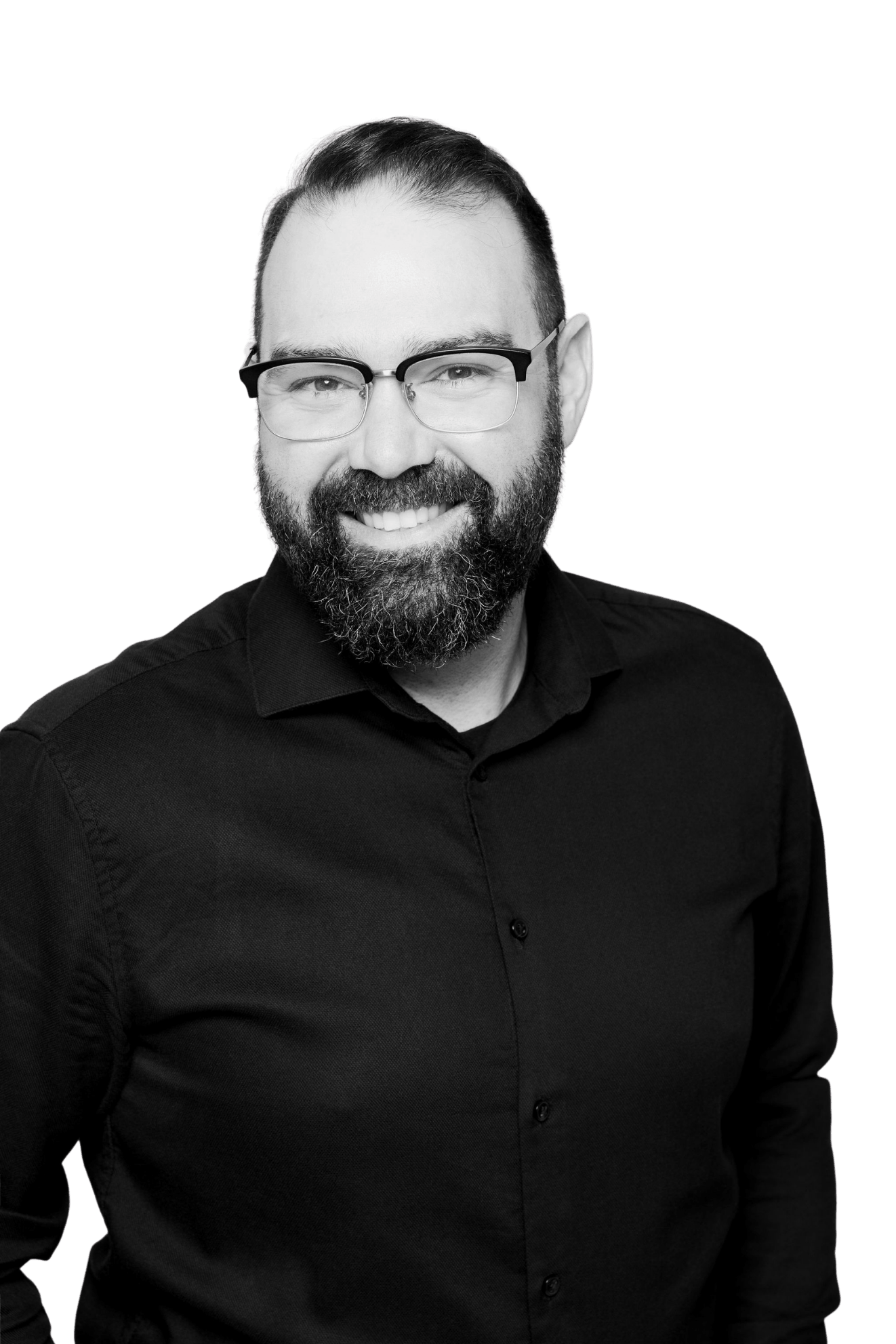 Black and white portrait of a man with glasses, a beard, short hair, wearing a black shirt, smiling against a black background.
