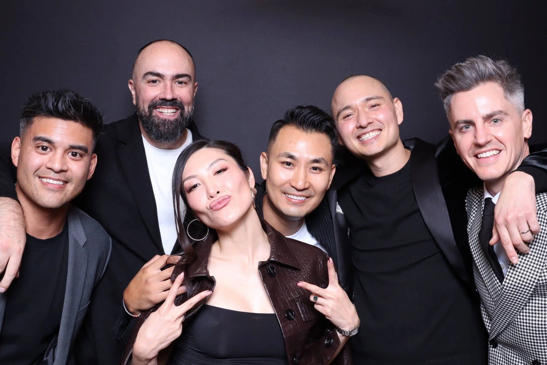 Group of six diverse smiling people posing together against a dark background.