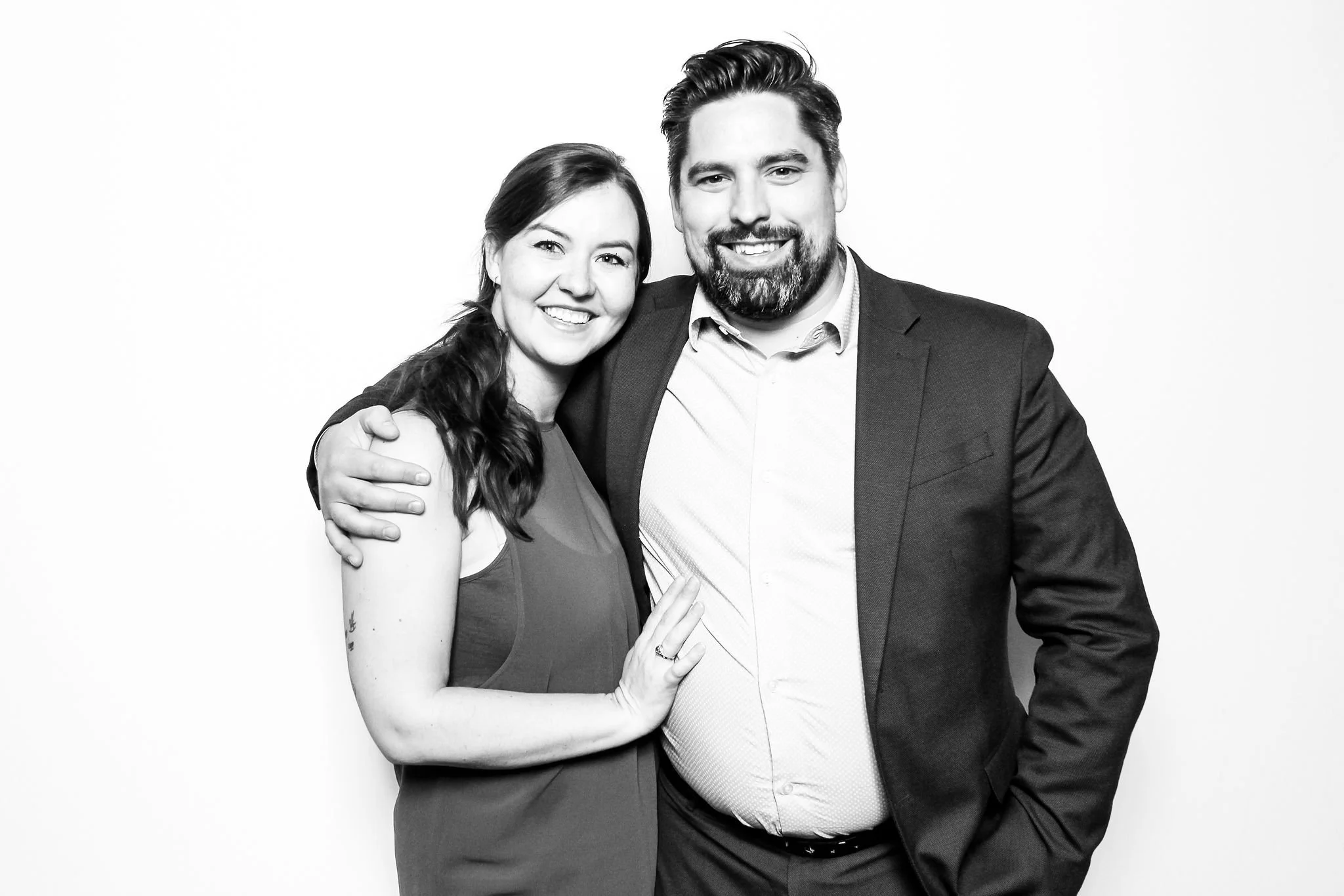 A happy couple in formal attire smiling and embracing for a photo in front of a plain white background.