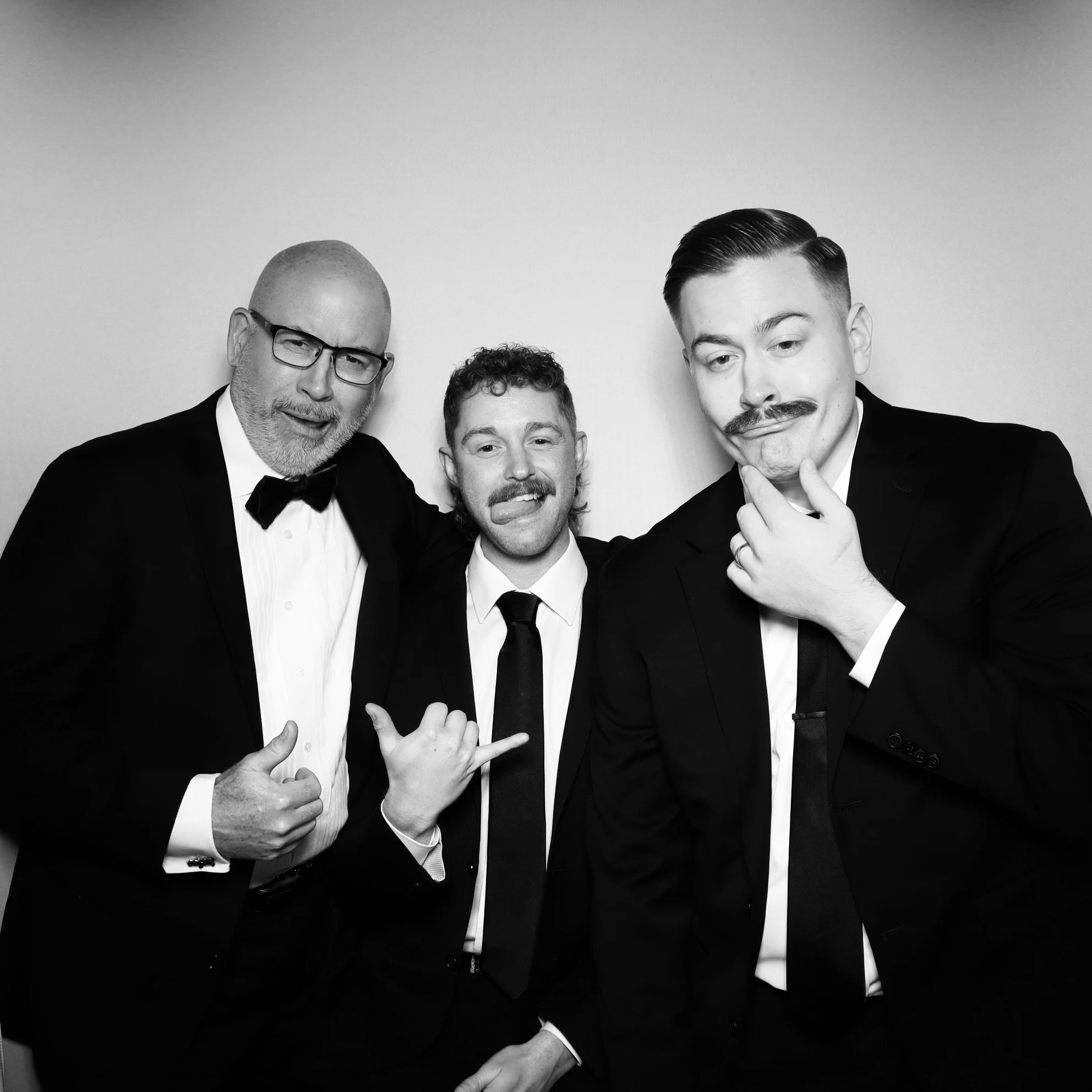 Three men in tuxedos making funny faces in a black and white photo.