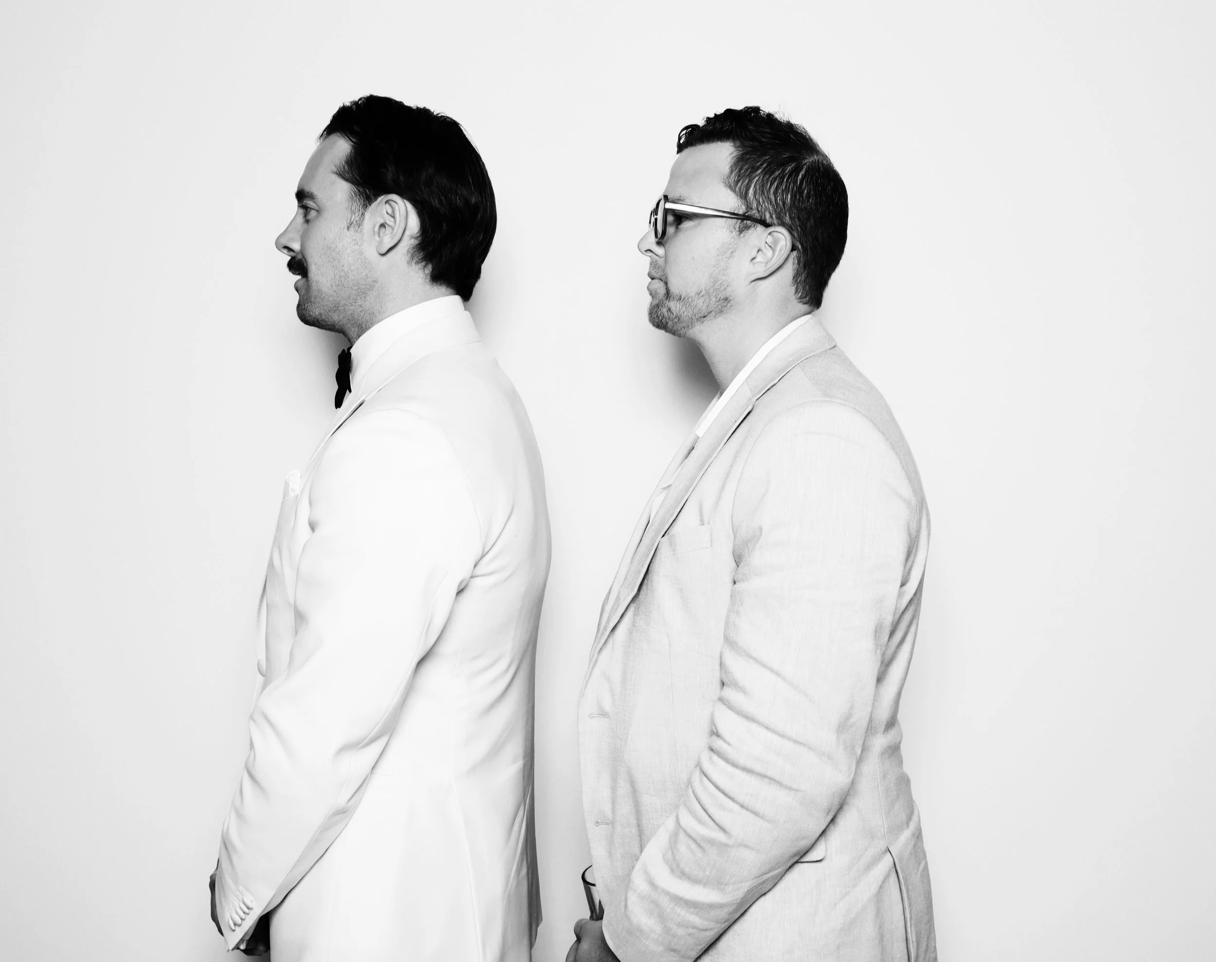 Two men dressed in suits standing side by side facing left in black and white photo.